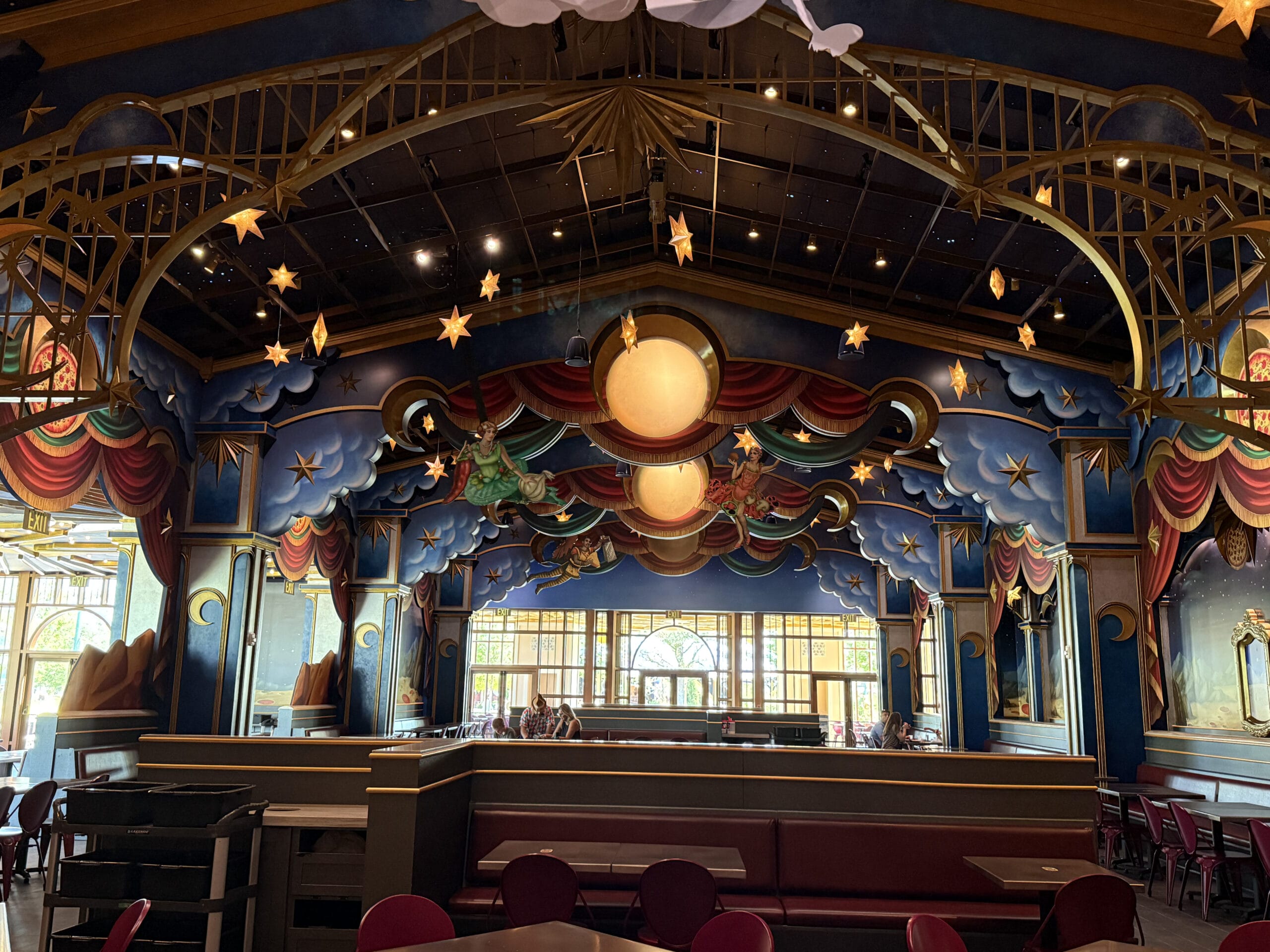 A whimsical Pizza Moon Restaurant interior with a starry sky, colorful drapes, and theatrical decor above dining tables.