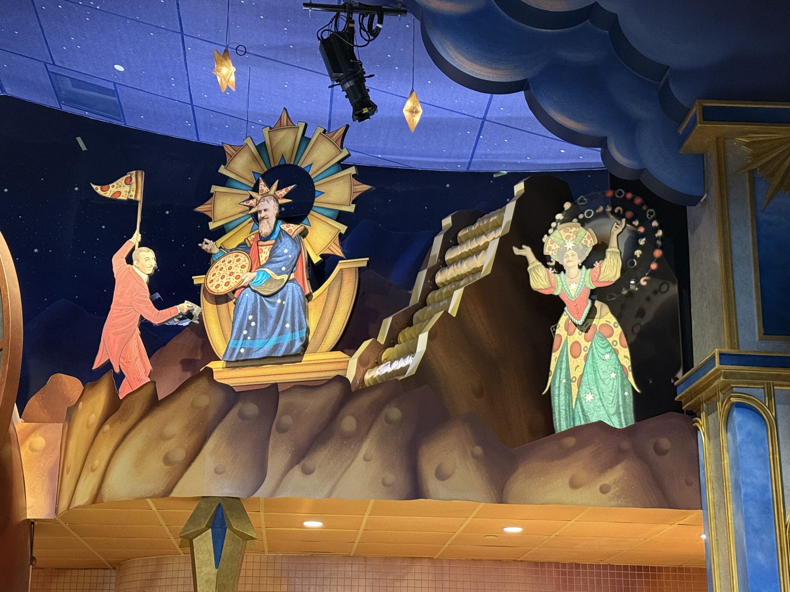Colorful mural at Pizza Moon Restaurant: a king, queen-like figure, and red-robed figure on a rocky, celestial background.