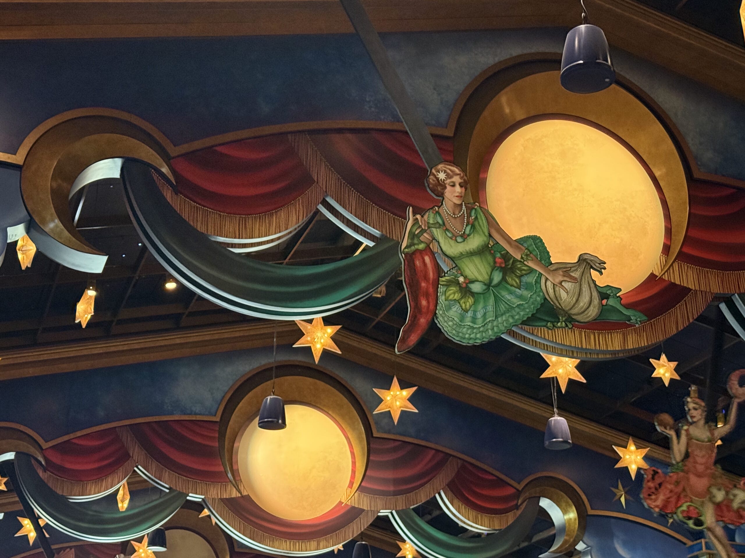Whimsical ceiling decor at Pizza Moon Restaurant with moons, stars, and a woman on a swing under draped red curtains.