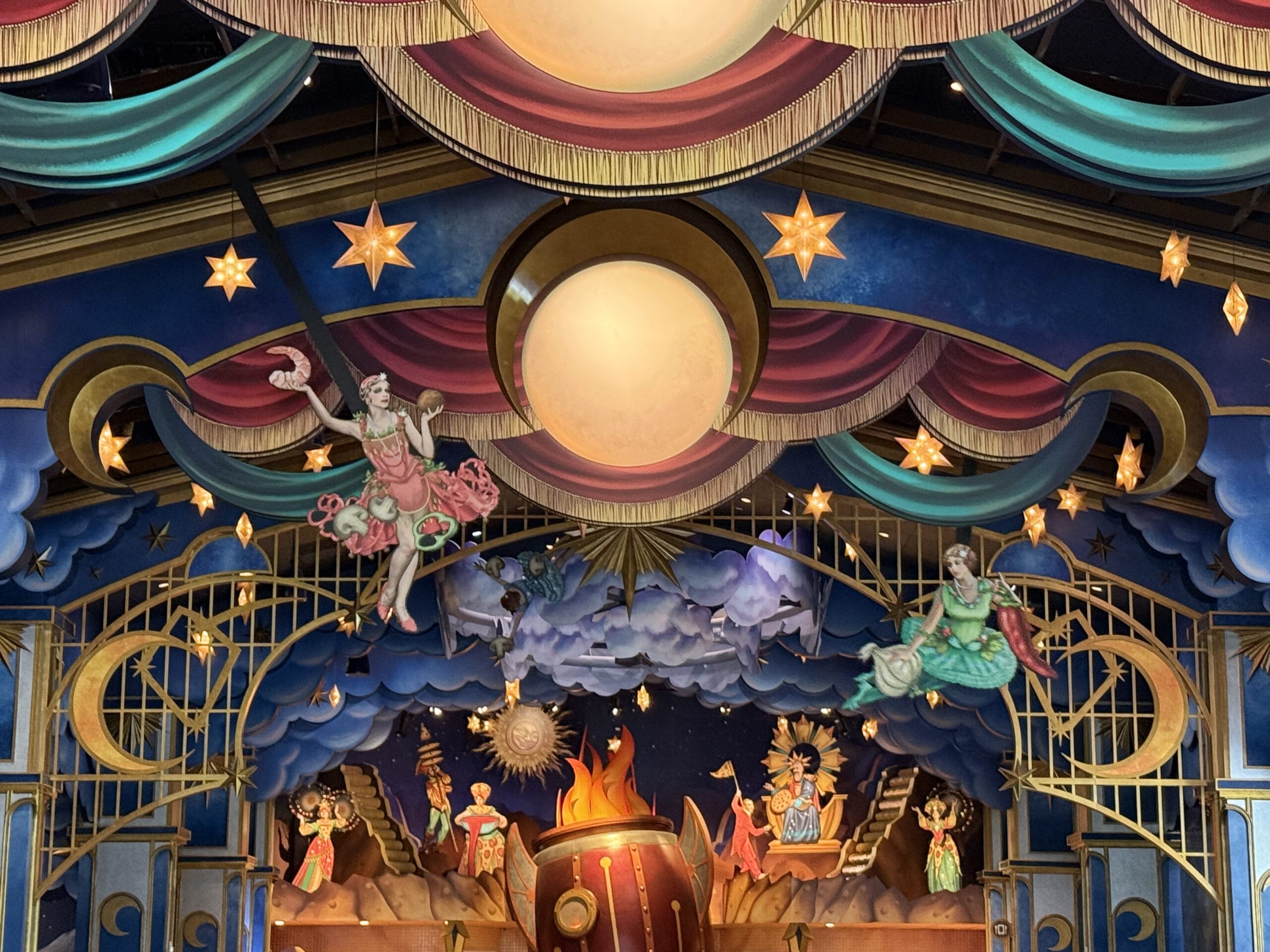 Colorful stage at Pizza Moon Restaurant in Celestial Park, with whimsical circus figures and acrobats above a lively scene.