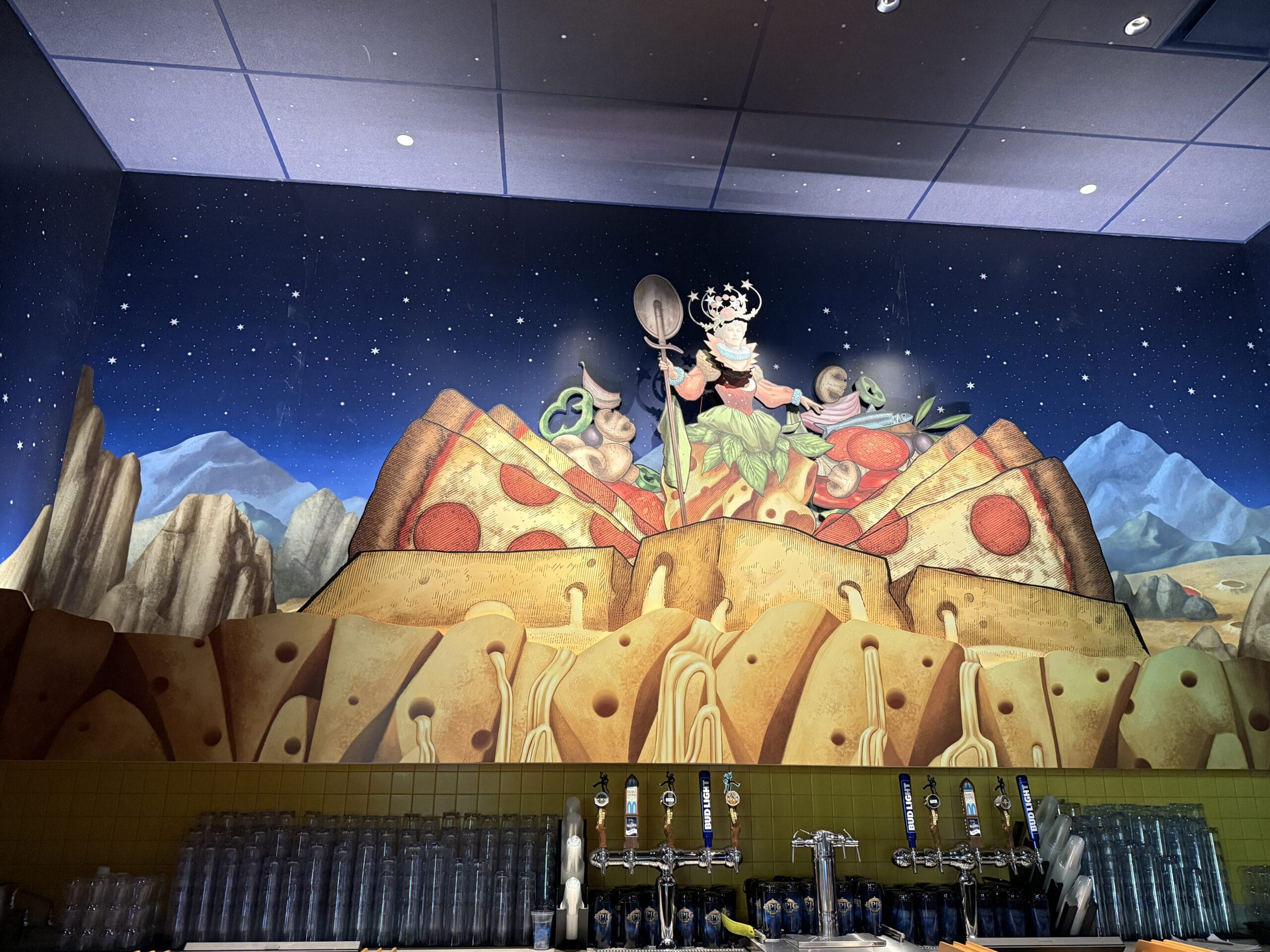 A mural shows a woman with utensils atop a Pizza Moon and cheese mountain beneath Celestial Park’s starry sky.