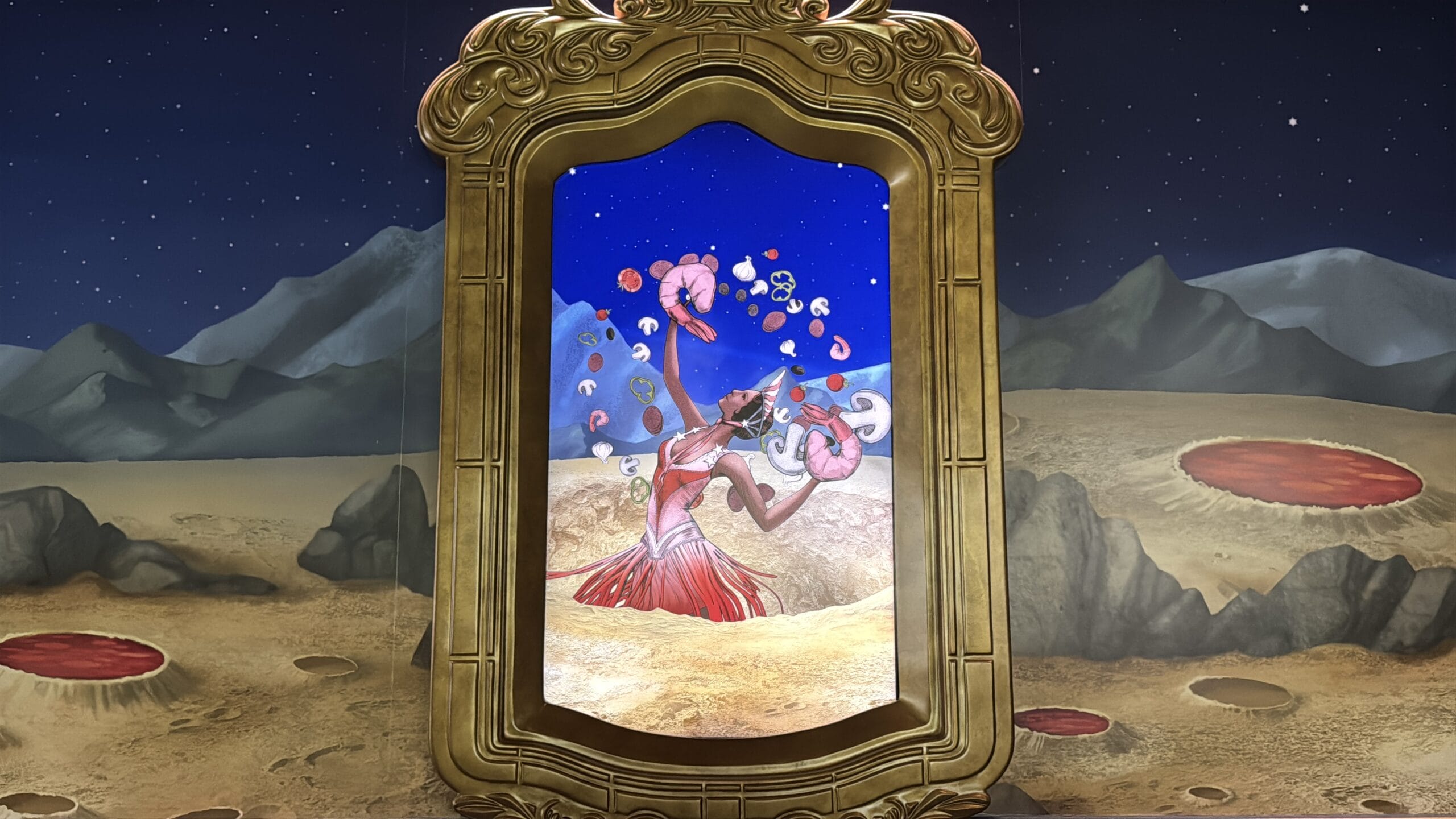 A framed artwork depicts a surreal, dog-headed figure in a desert under Epic Universe mountains and floating pink objects.