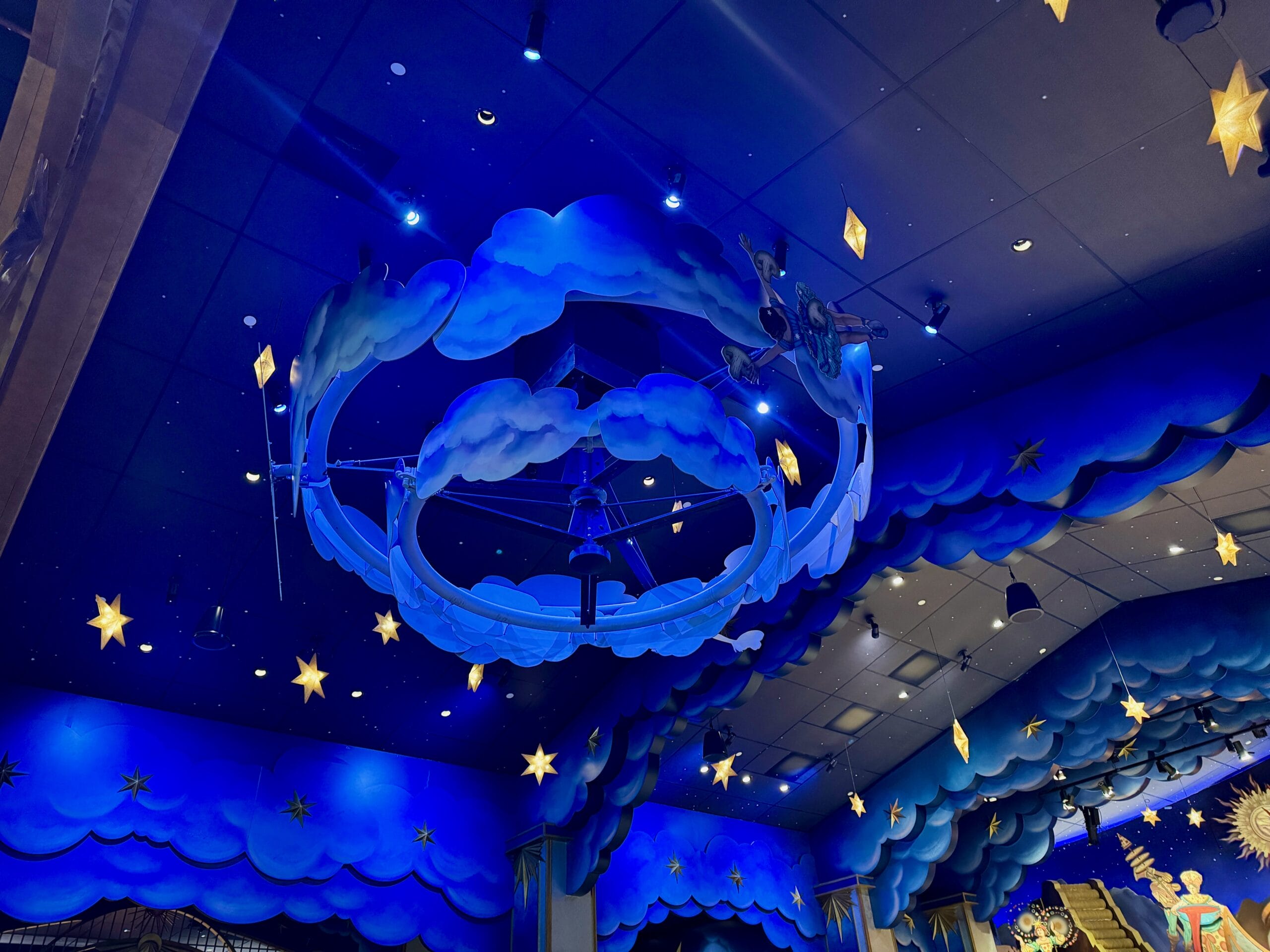 Blue ceiling with cloud and star decor, blue lights, creating a whimsical night sky at Epic Universe’s Celestial Park.