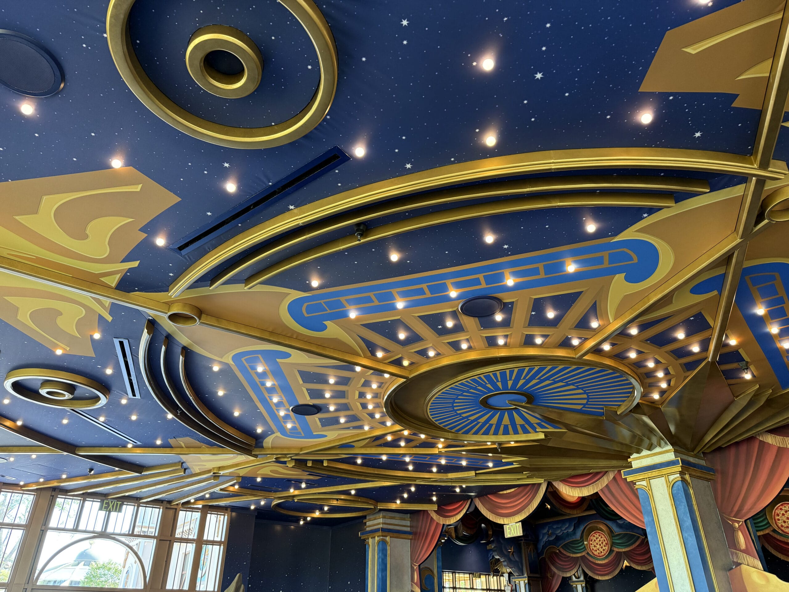 A colorful, ornate ceiling at Pizza Moon Restaurant in Celestial Park, with gold-blue patterns and star-like lights above.