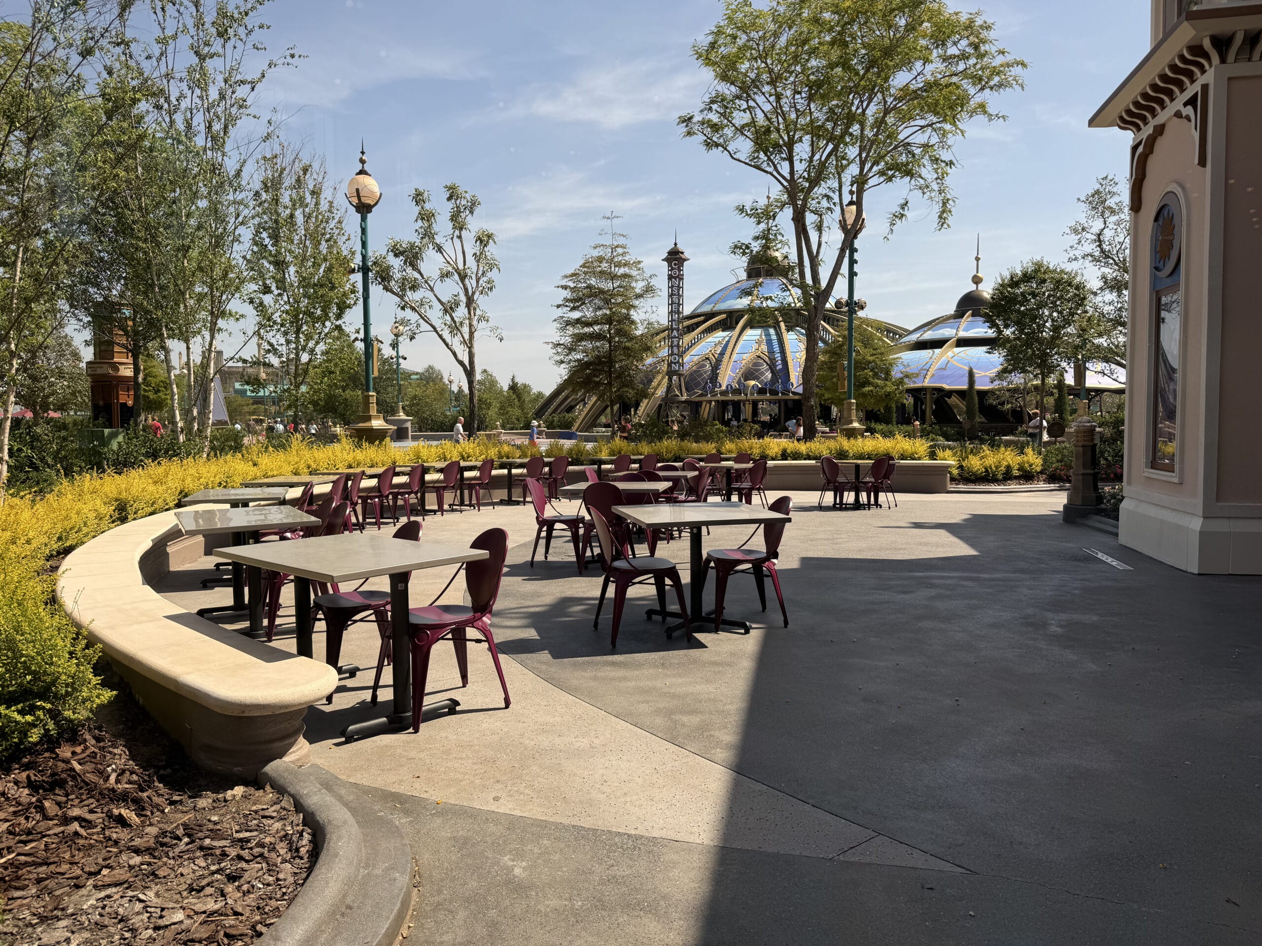 Outdoor seating at Pizza Moon Restaurant with empty tables, surrounded by trees and yellow shrubs in Celestial Park.
