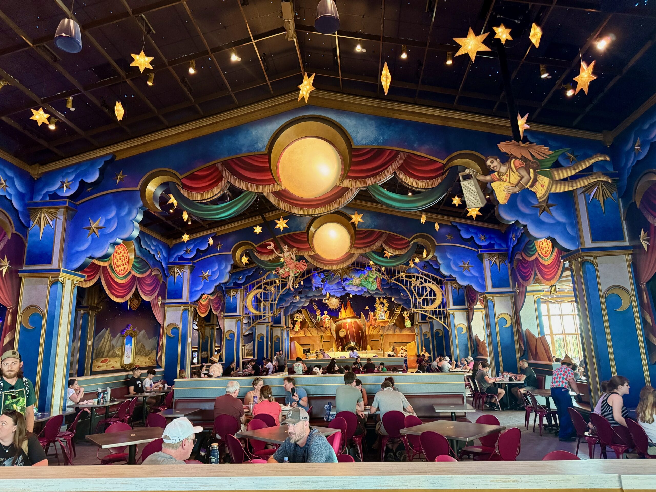 Themed restaurant at Epic Universe’s Celestial Park with whimsical decor, hanging stars, and pizza at Pizza Moon Restaurant.