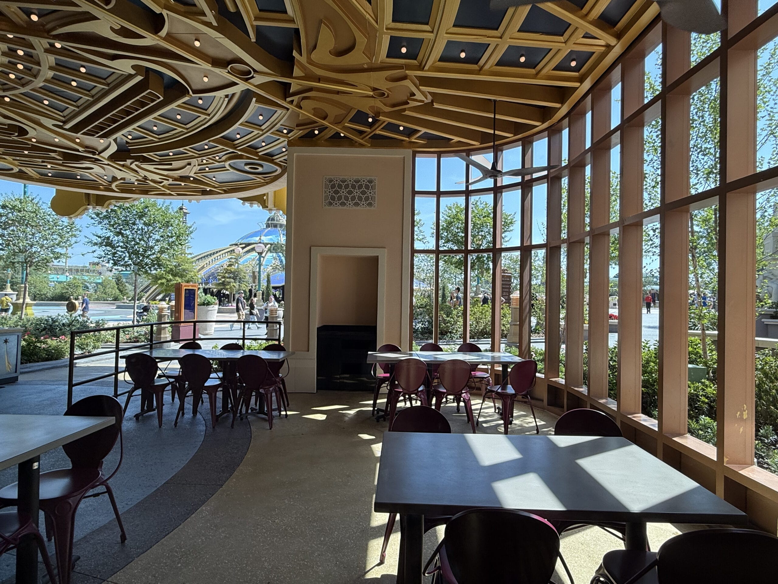 Sunlit café at Pizza Moon Restaurant with empty tables, ornate ceiling, and views of Celestial Park outside.