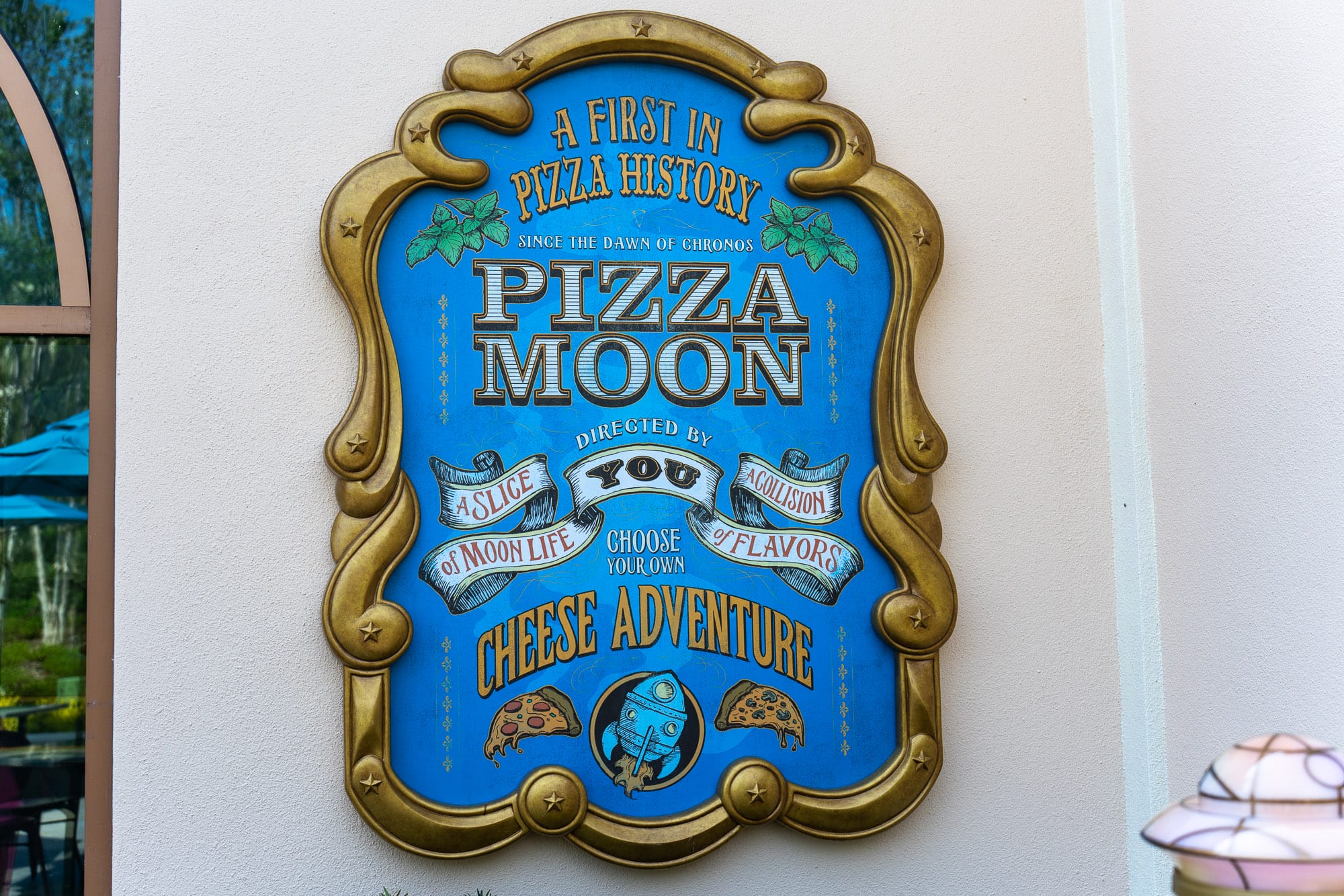 Blue and gold sign reads: "Pizza Moon Restaurant—a cheese adventure at Celestial Park. Choose your own sauces and flavors.