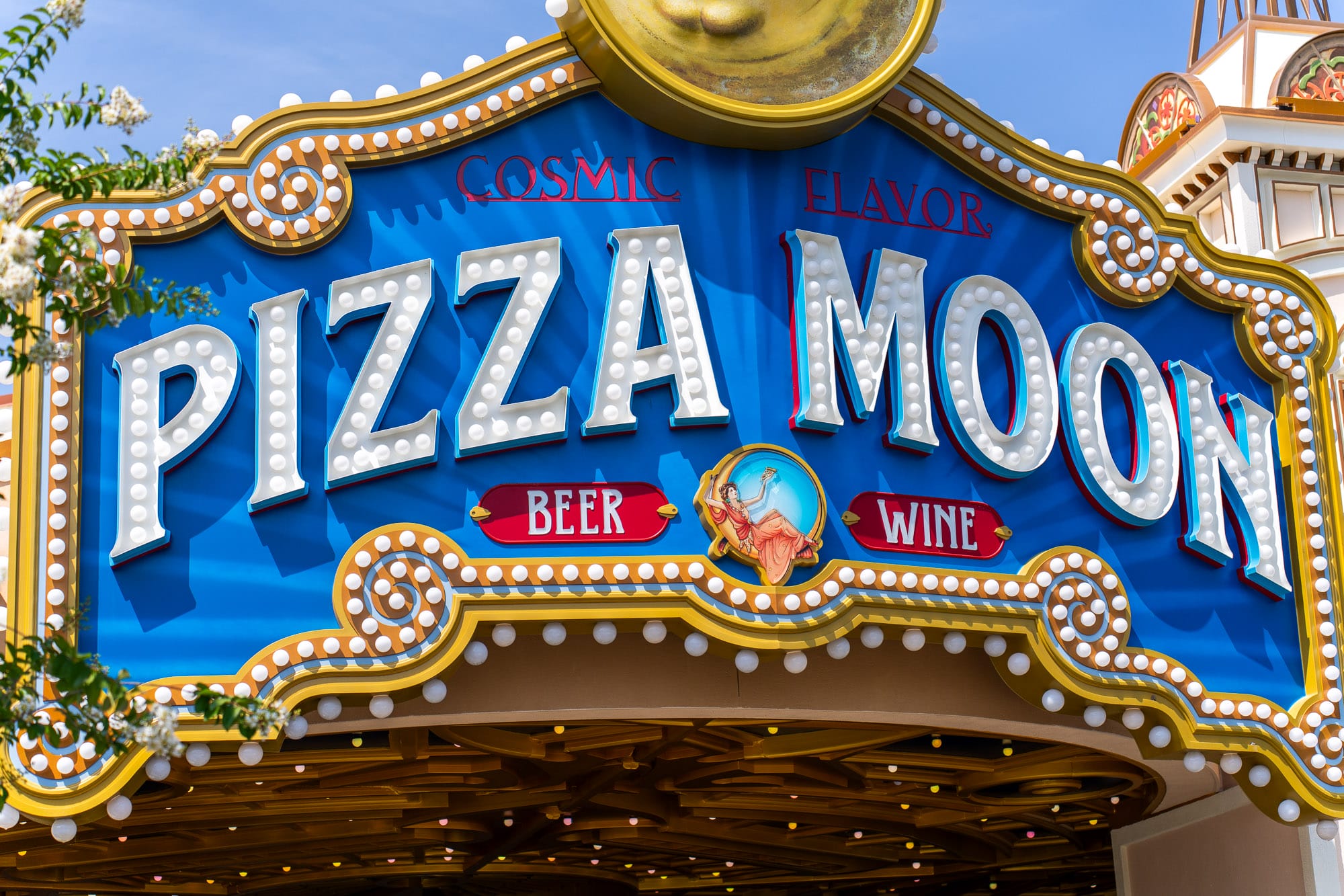 Blue and gold "Pizza Moon Restaurant" sign lights up Celestial Park at Epic Universe, offering cosmic flavor, beer, and wine.