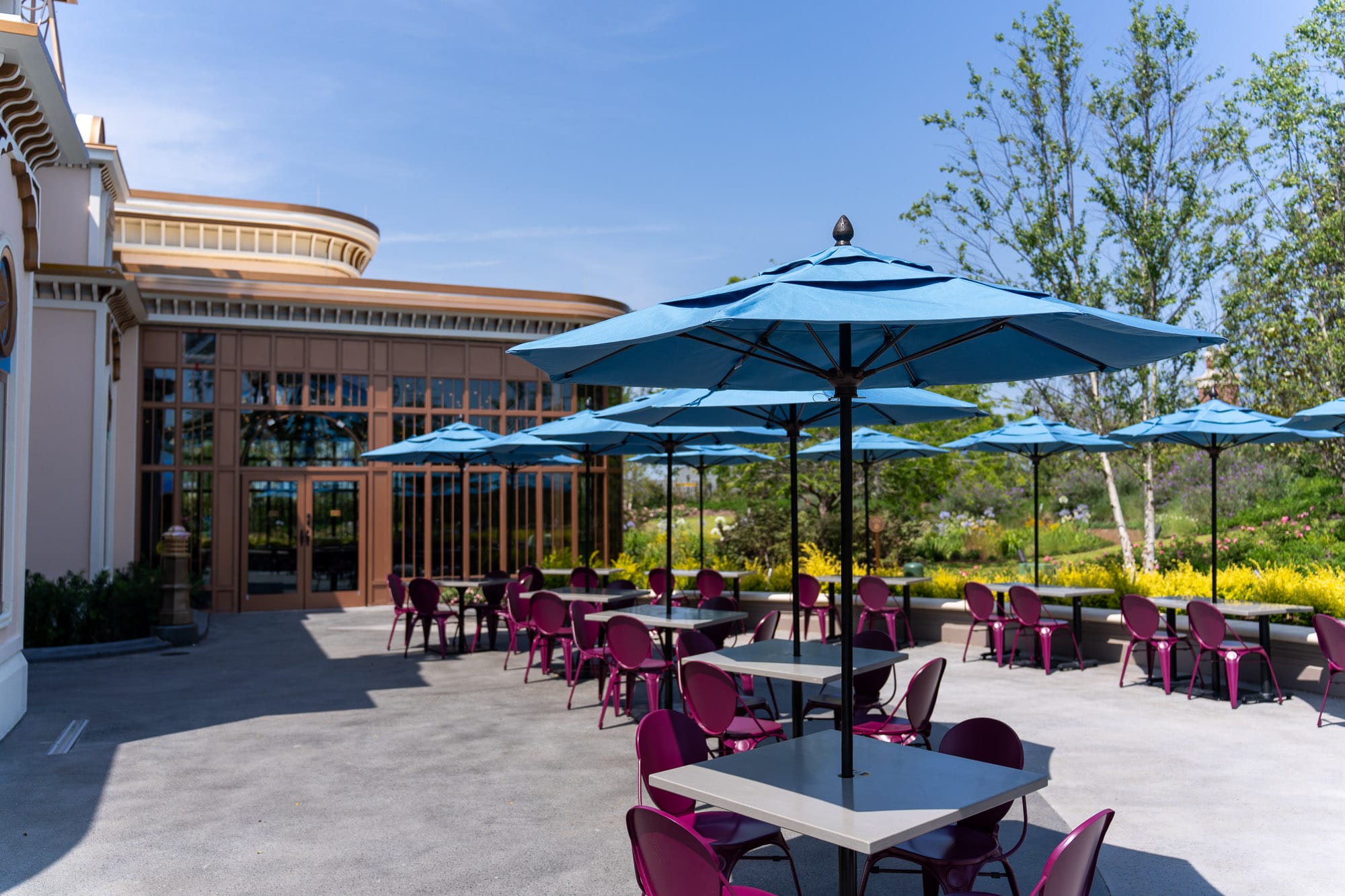 Outdoor patio at Pizza Moon Restaurant with purple chairs and blue umbrellas in Celestial Park on a sunny day.