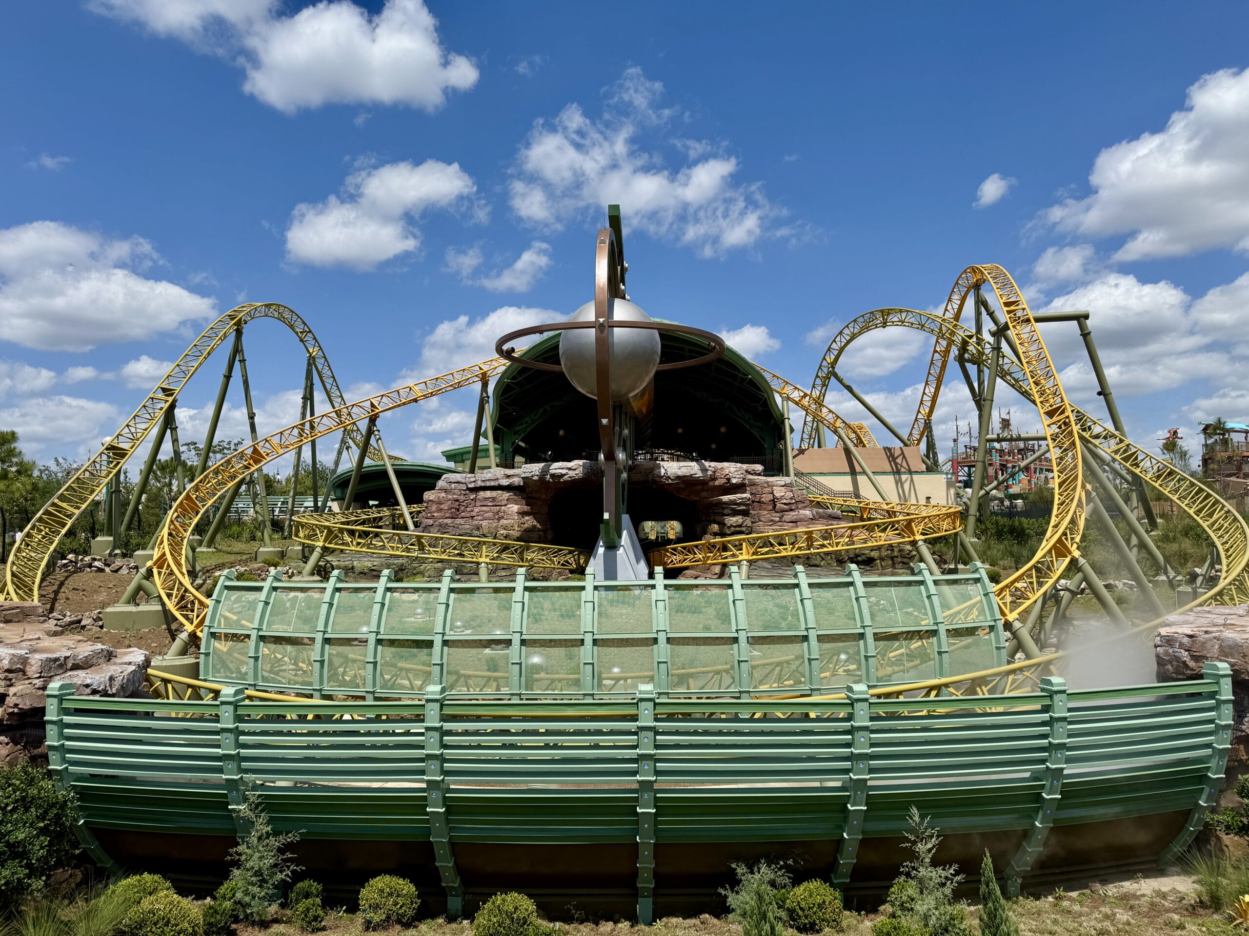 Bright yellow Stardust Racers roller coaster with loops and turns, green and metal structure under a blue sky.