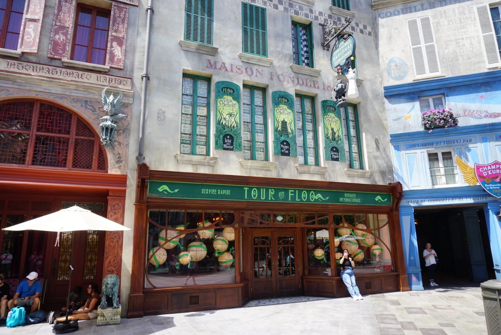 People gather outside a whimsical Parisian-style cafe with green accents near Epic Universe and Wizarding World attractions.