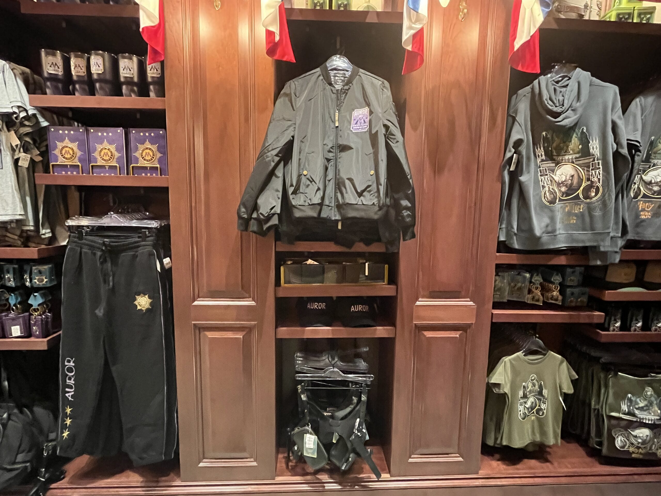Shelves display Epic Universe Harry Potter Auror-themed merchandise, including a jacket, pants, hoodies, and accessories.