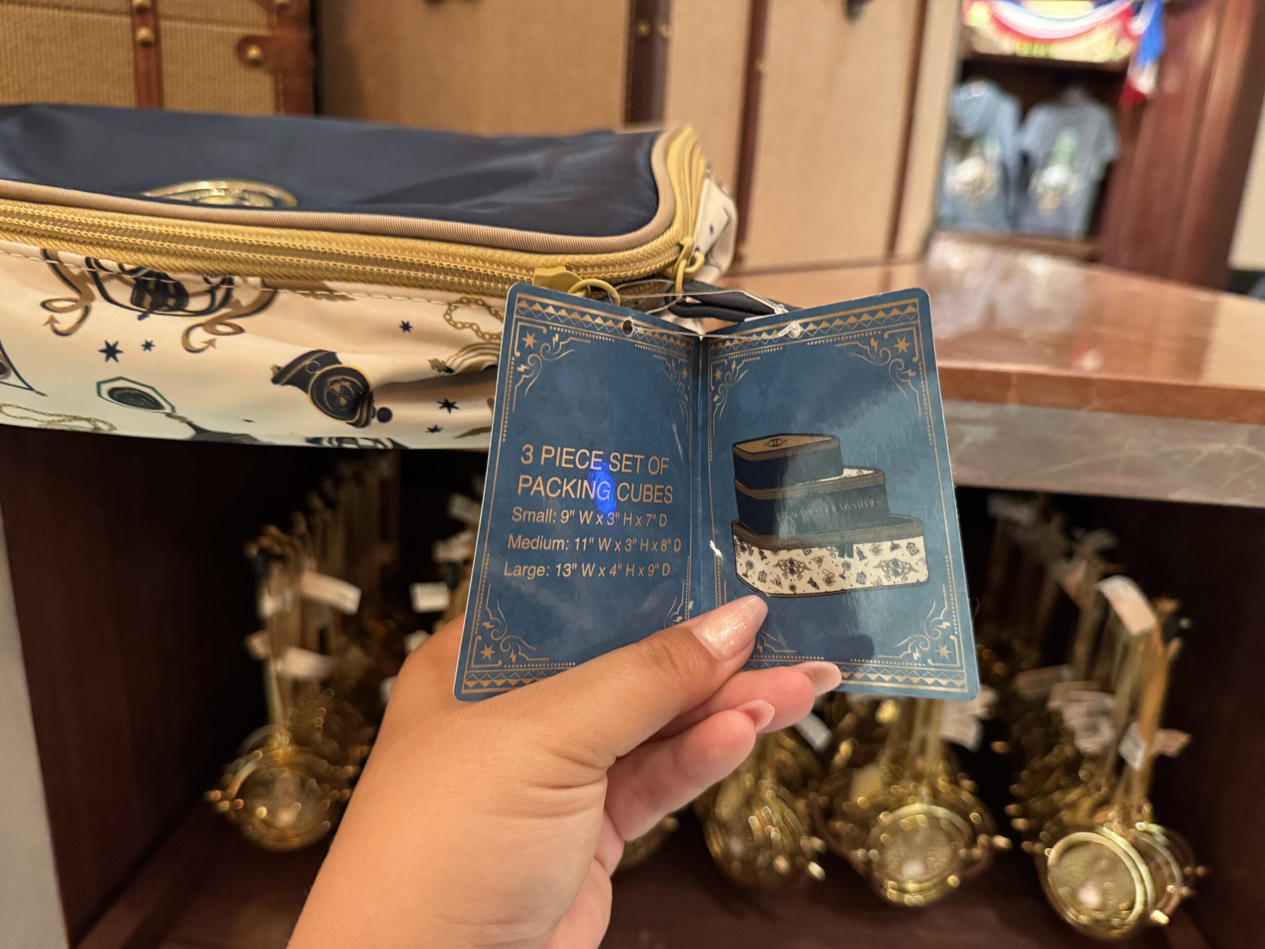 A hand holds a tag for 3-piece packing cubes before shelves of Wizarding World of Harry Potter merchandise.