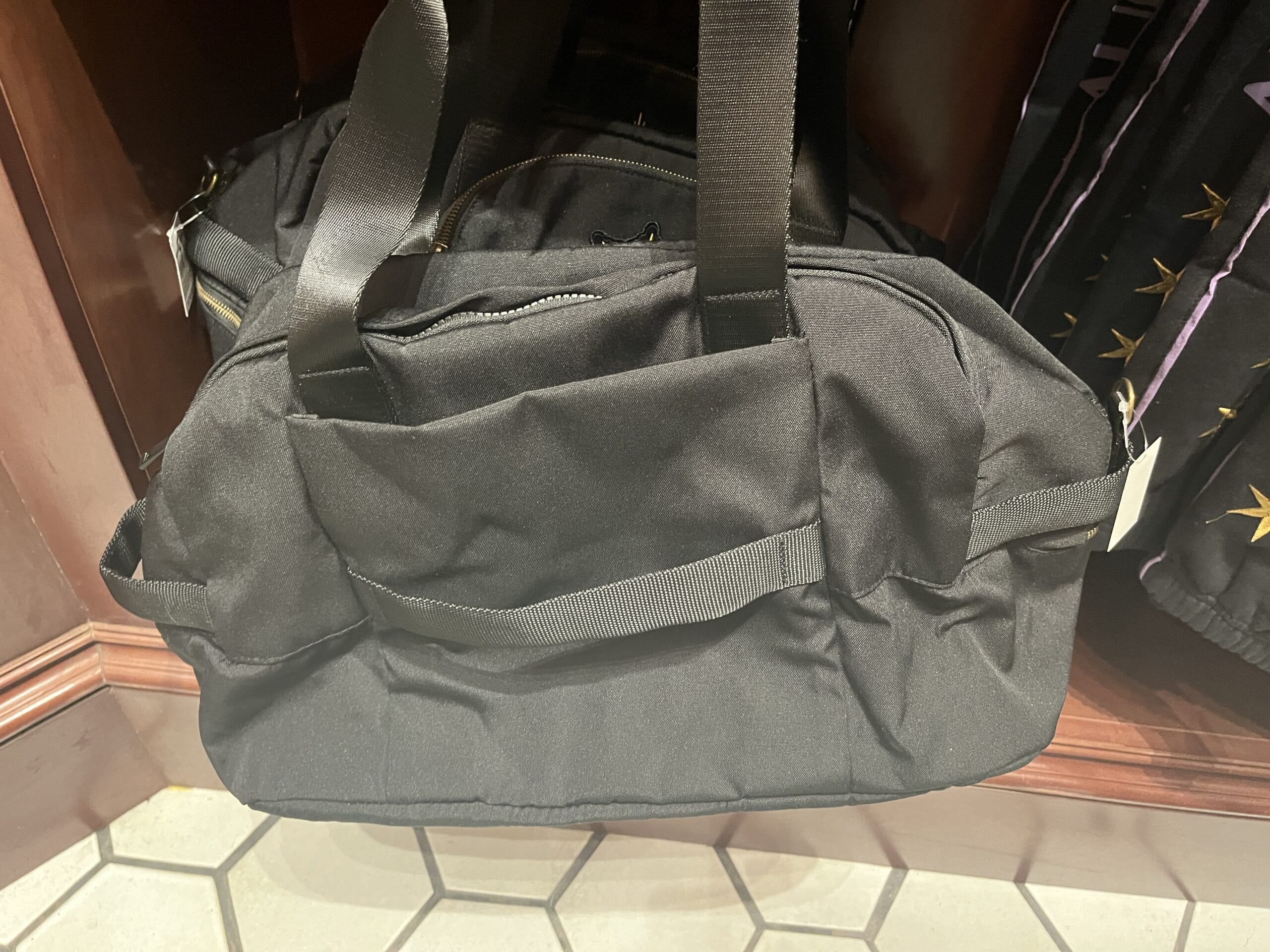 A plain black duffel bag with handles sits on a wooden shelf—perfect for Wizarding World Harry Potter merchandise.