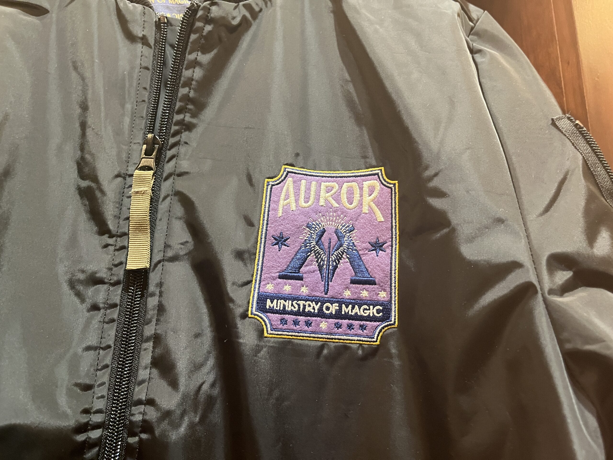 Black jacket with a purple "Auror, Ministry of Magic" patch—perfect Wizarding World merchandise for any Harry Potter fan.