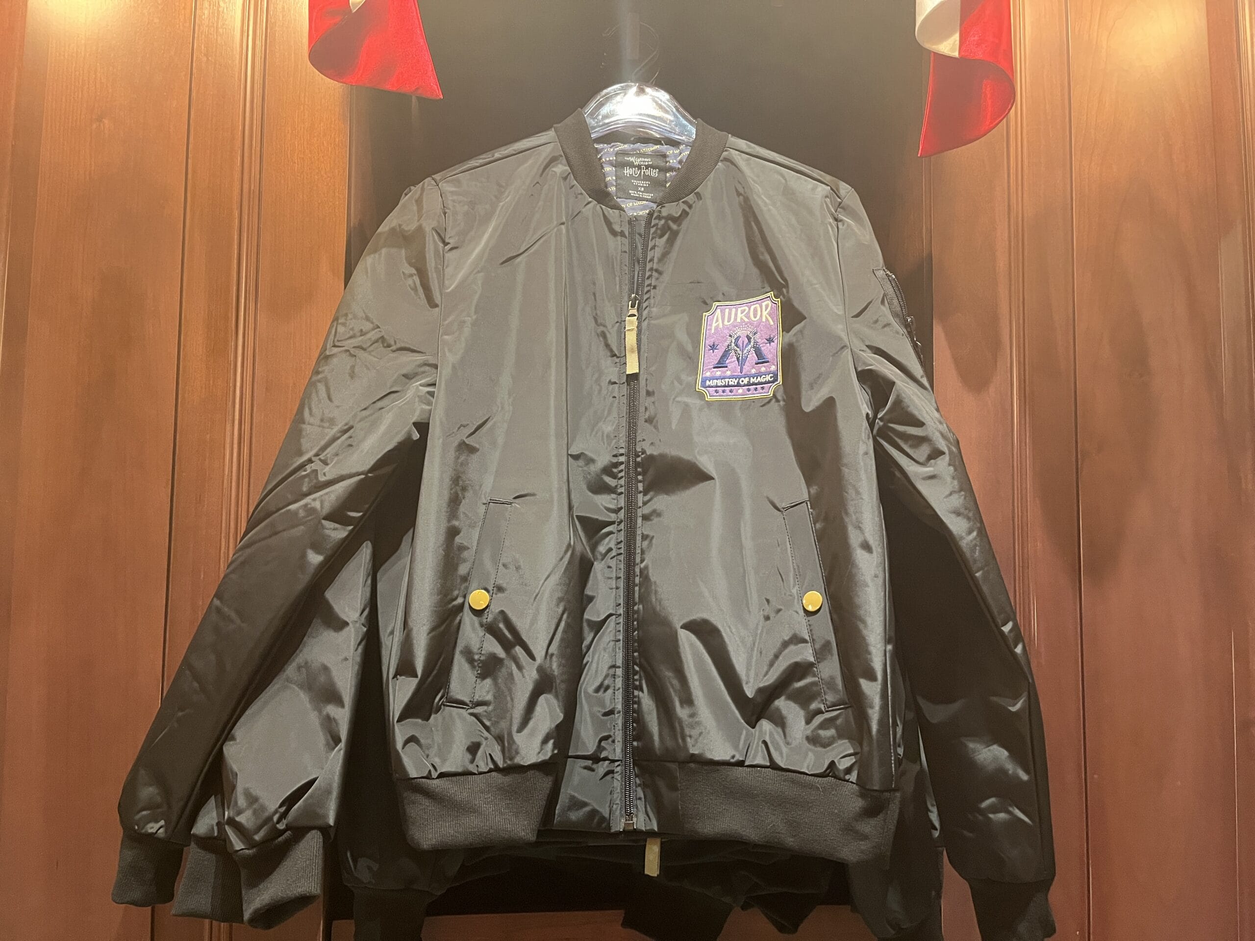 A shiny black bomber jacket with yellow buttons and a purple "Auror" patch—perfect Harry Potter merchandise—hangs on a wall.