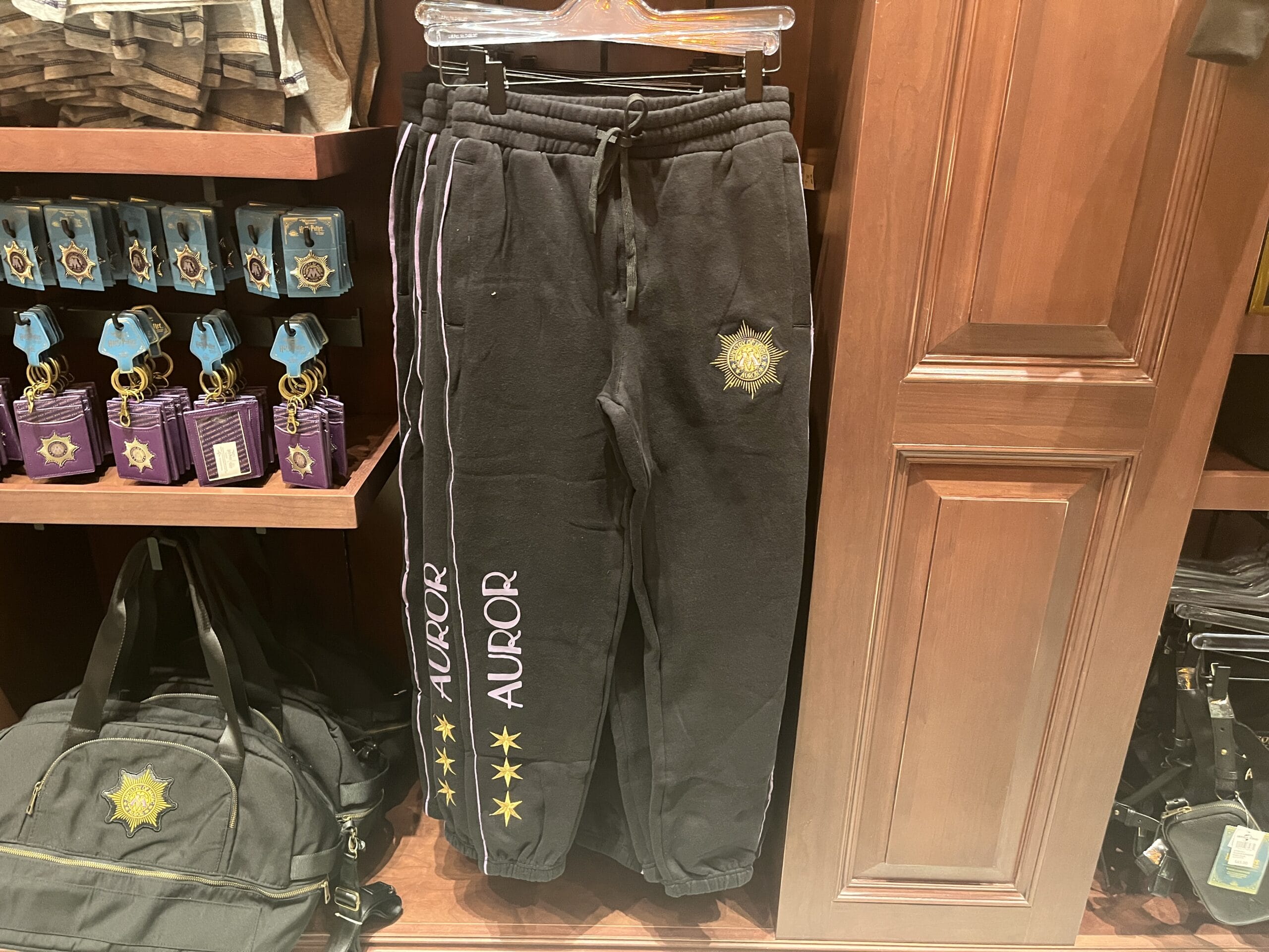 Black sweatpants with "AUROR" and gold stars, like Wizarding World of Harry Potter merchandise, hang next to matching items.