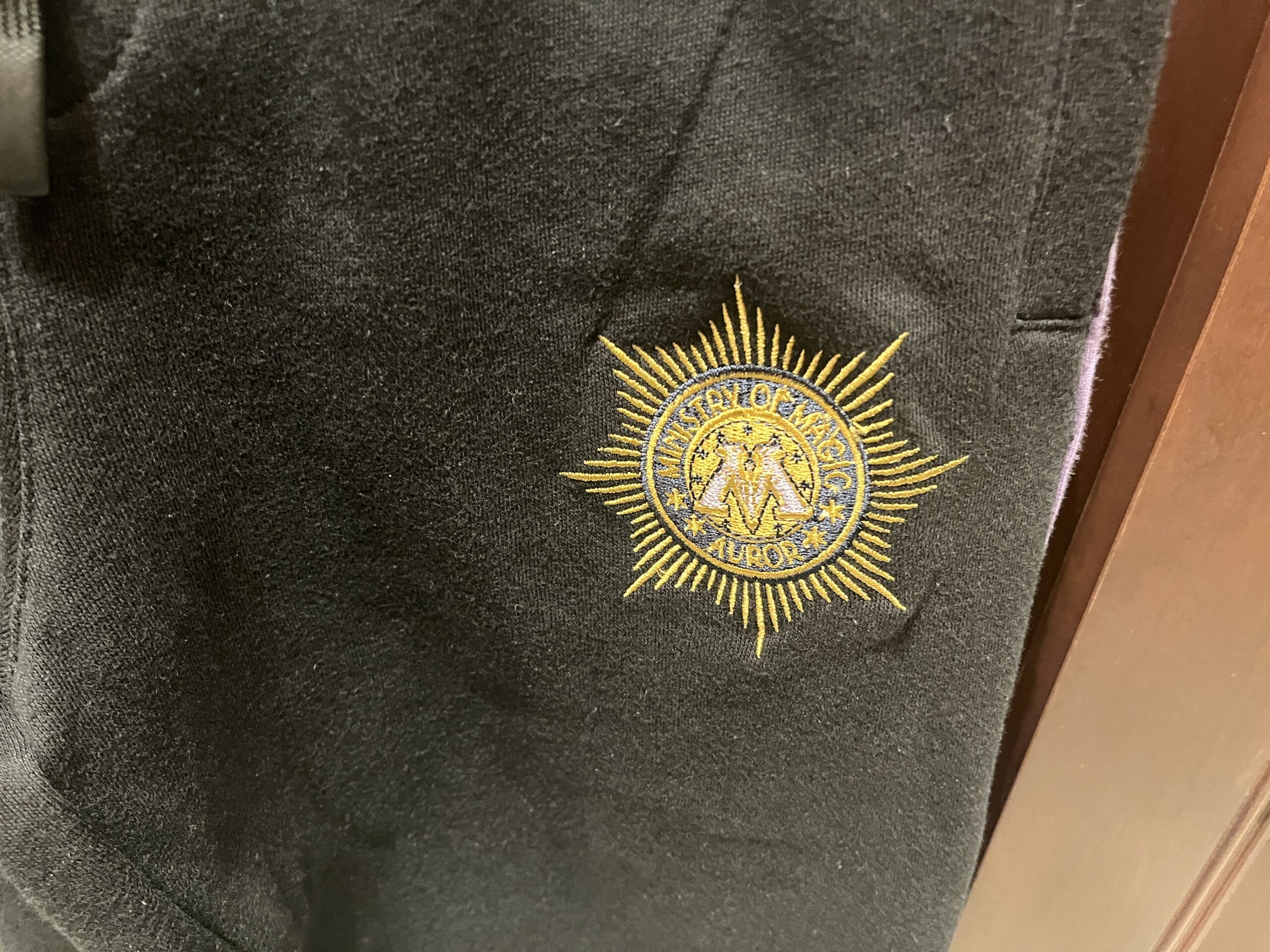 Black fabric with an embroidered yellow "Ministry of Magic Auror" emblem—perfect Harry Potter merchandise for any fan.