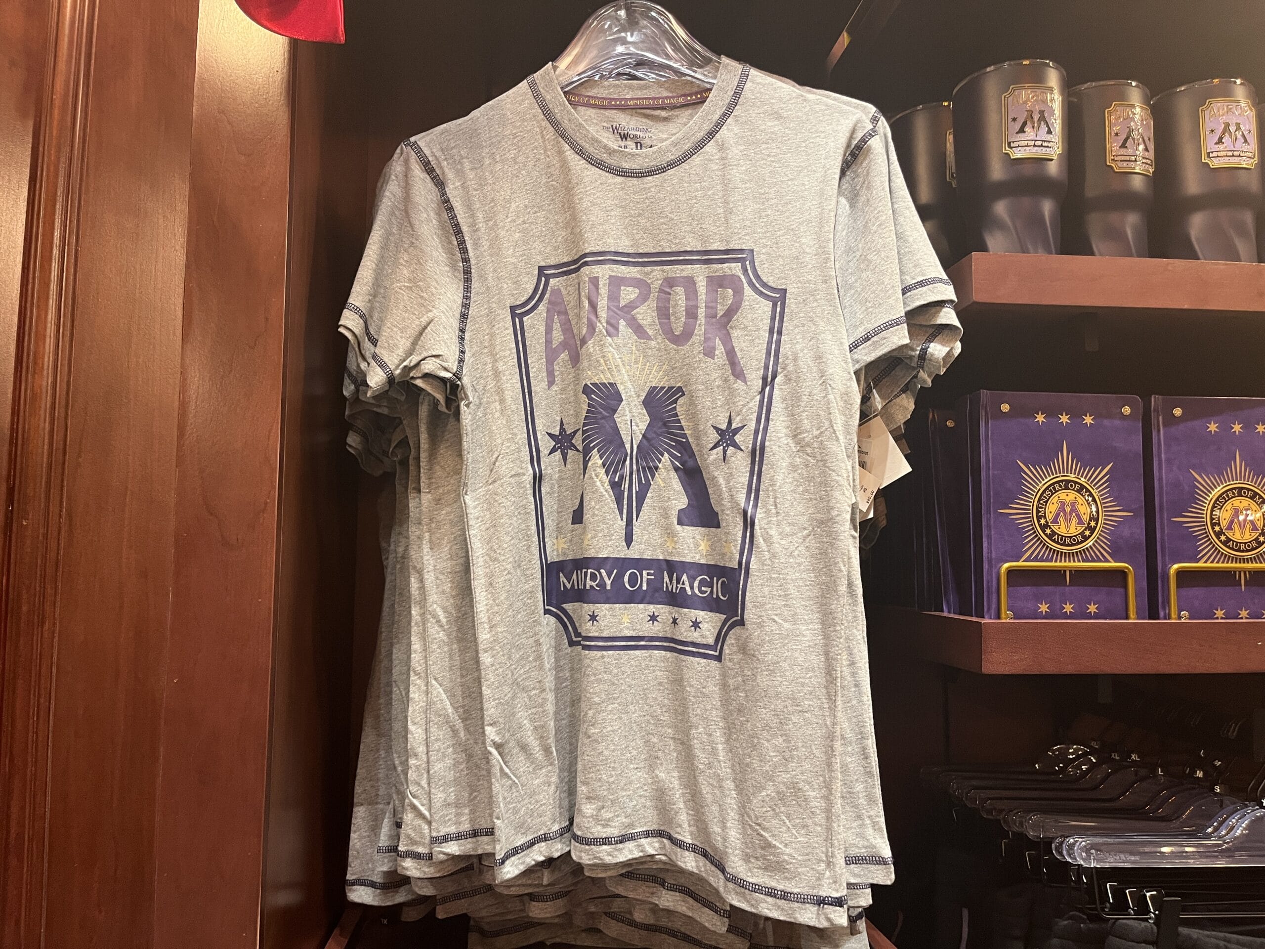 Gray T-shirt with "MIRY OF MAGIC," inspired by Wizarding World of Harry Potter merchandise, displayed on a store rack.