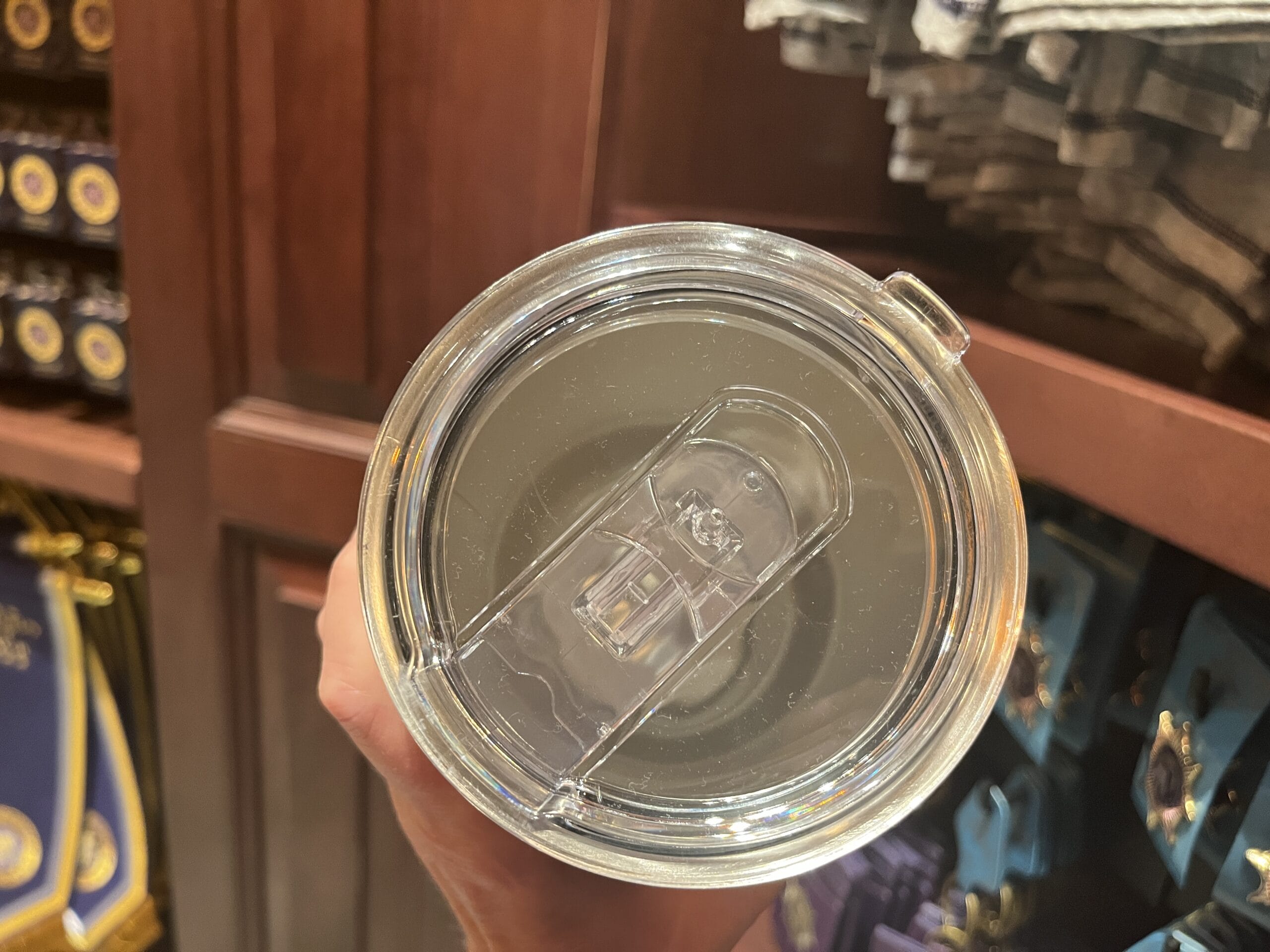 A hand holds a clear tumbler amid wooden shelves lined with Wizarding World of Harry Potter merchandise.