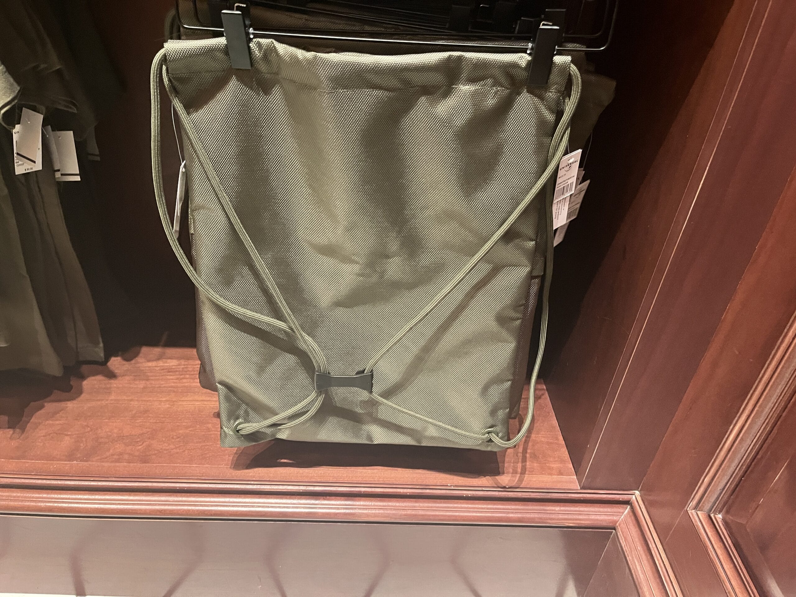 Olive green drawstring backpack with black clasps, inspired by Wizarding World of Harry Potter merchandise, on a wooden shelf.
