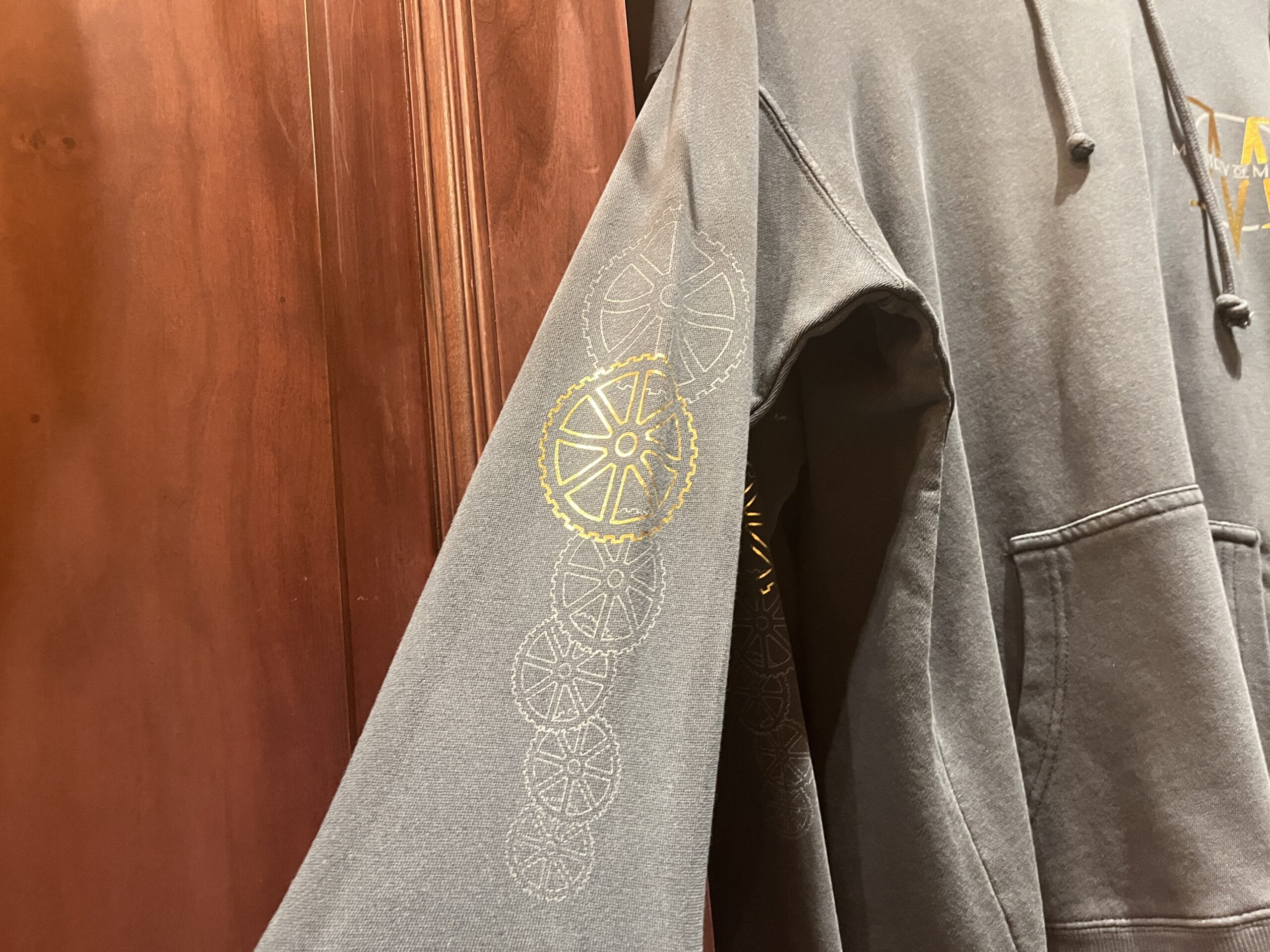 A gray hoodie with yellow and white gear designs—Epic Universe merchandise—hangs on a wooden door.