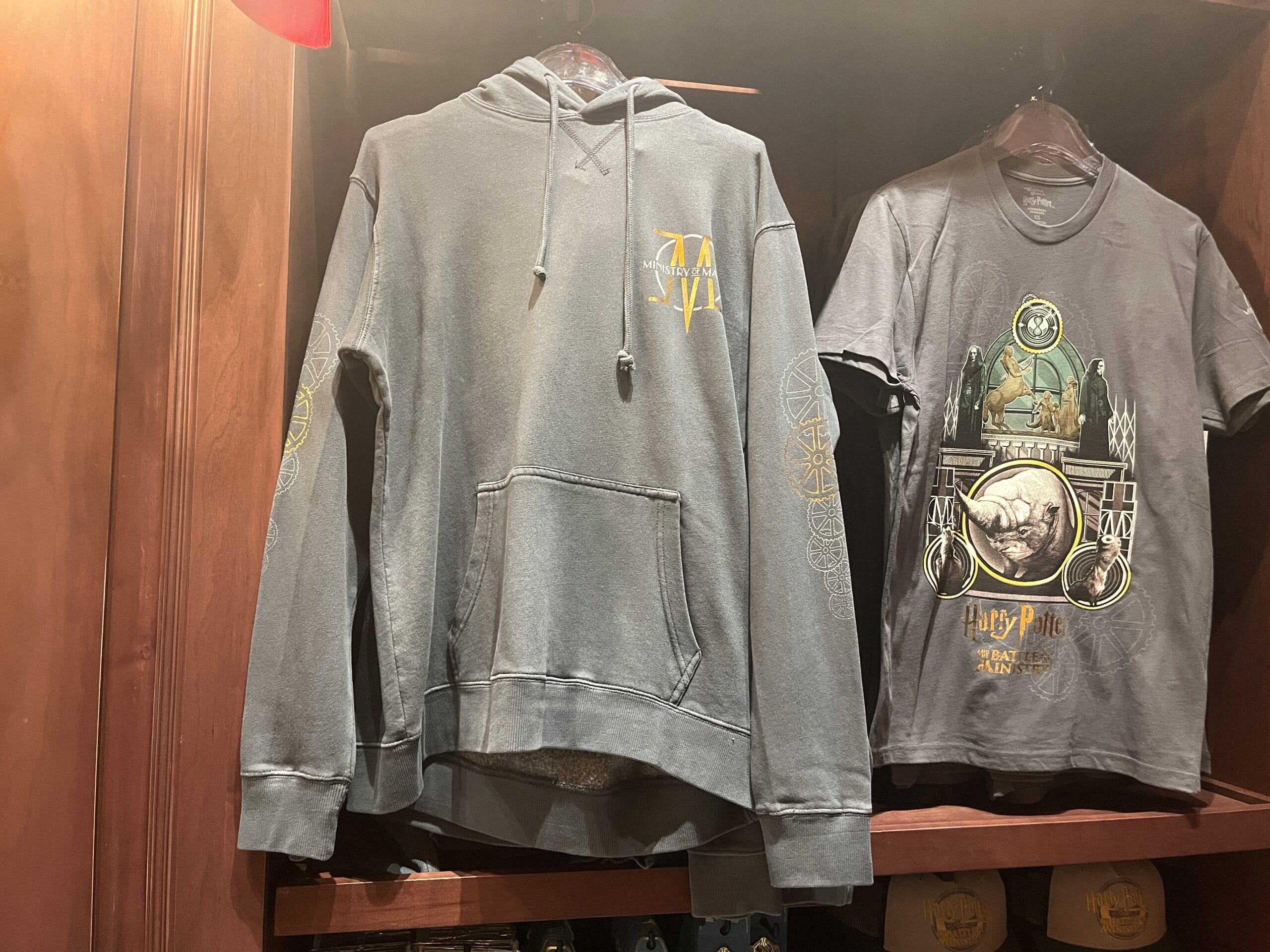 Gray hoodie and graphic tee with fantasy designs, perfect for fans of Wizarding World merchandise, hang on a wooden shelf.