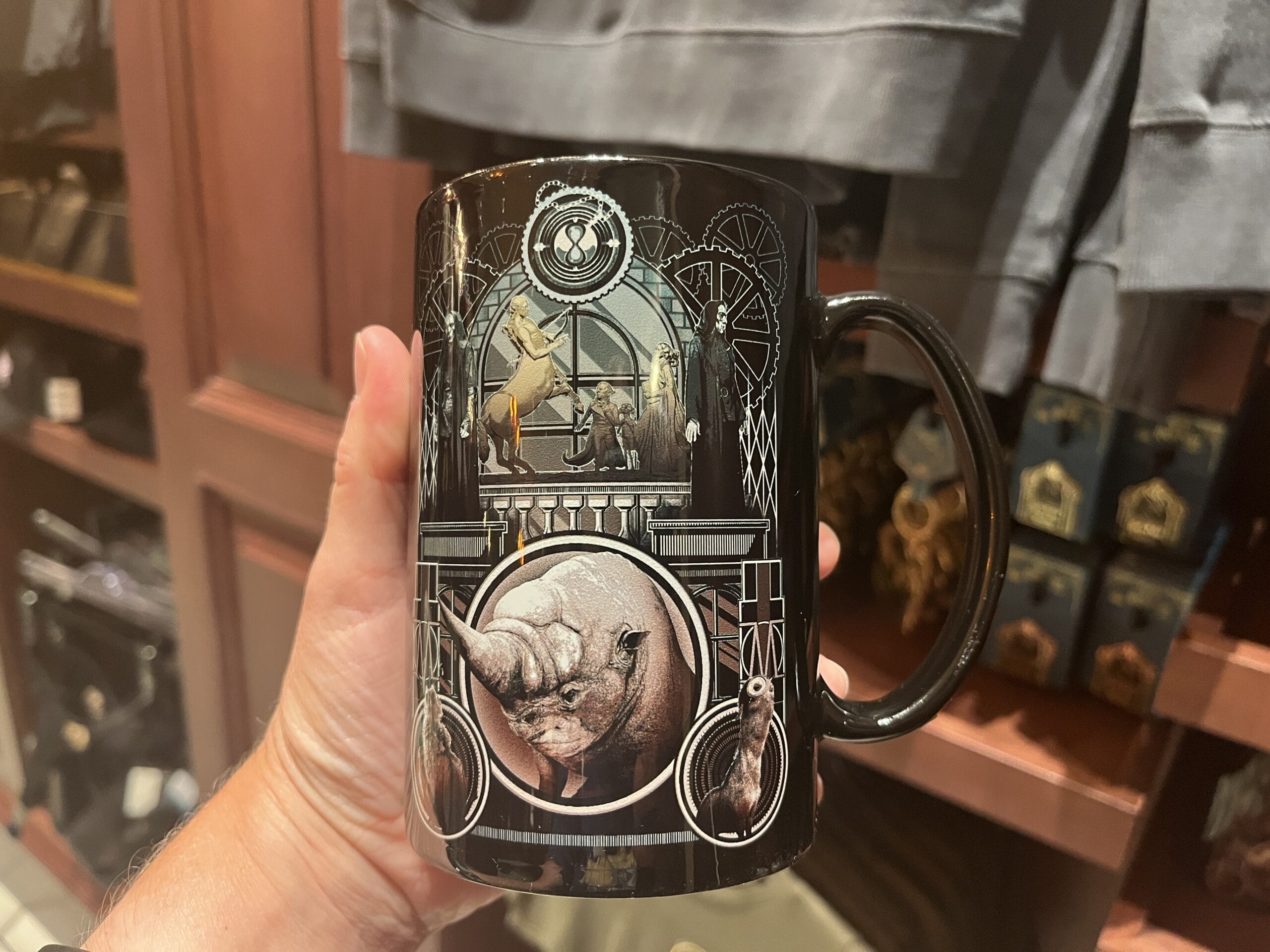A hand holds a black mug with intricate designs, perfect for Epic Universe or Wizarding World of Harry Potter merchandise prices.
