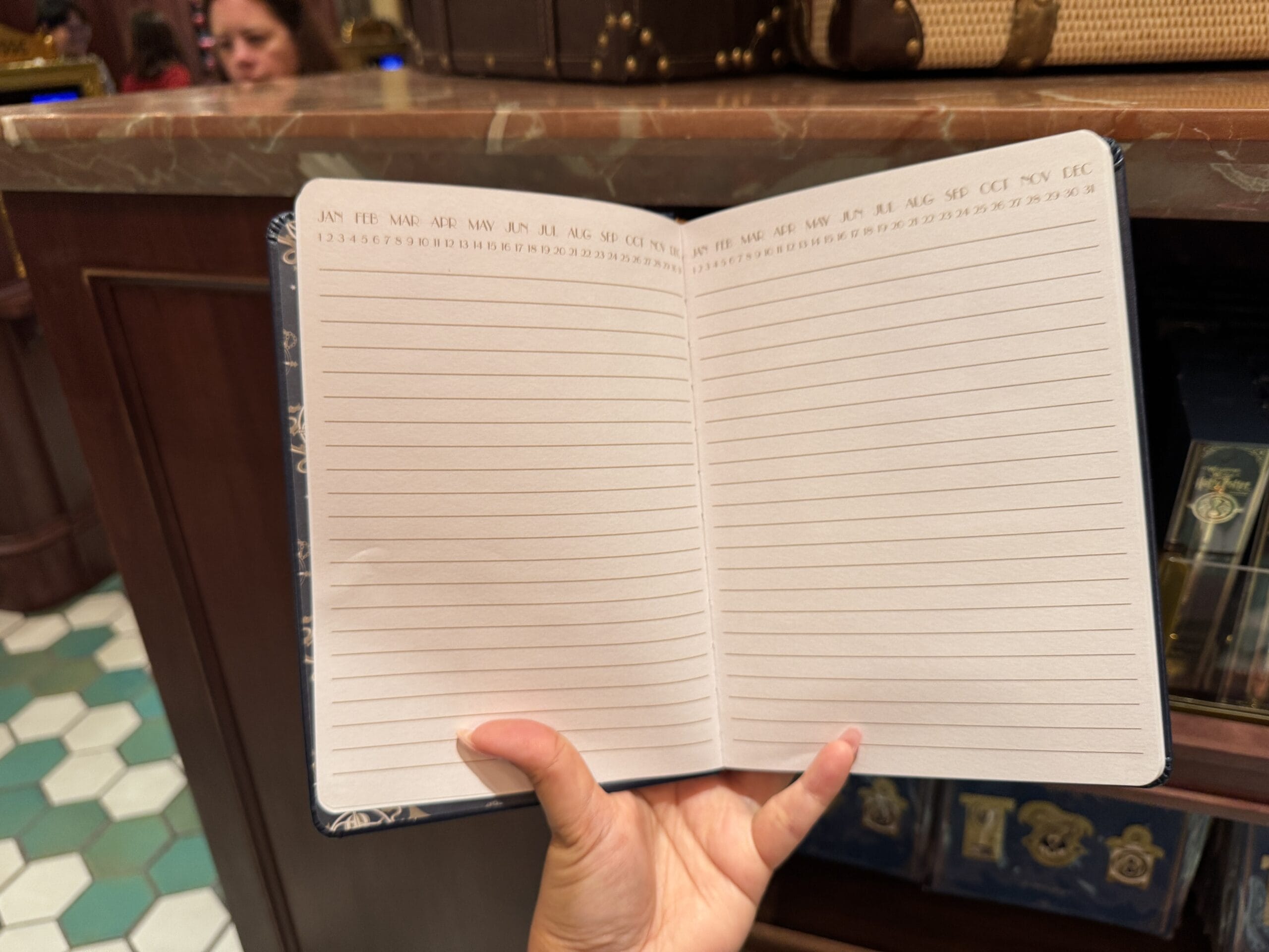 A hand opens a blank lined notebook with months and dates, inspired by Wizarding World of Harry Potter merchandise.