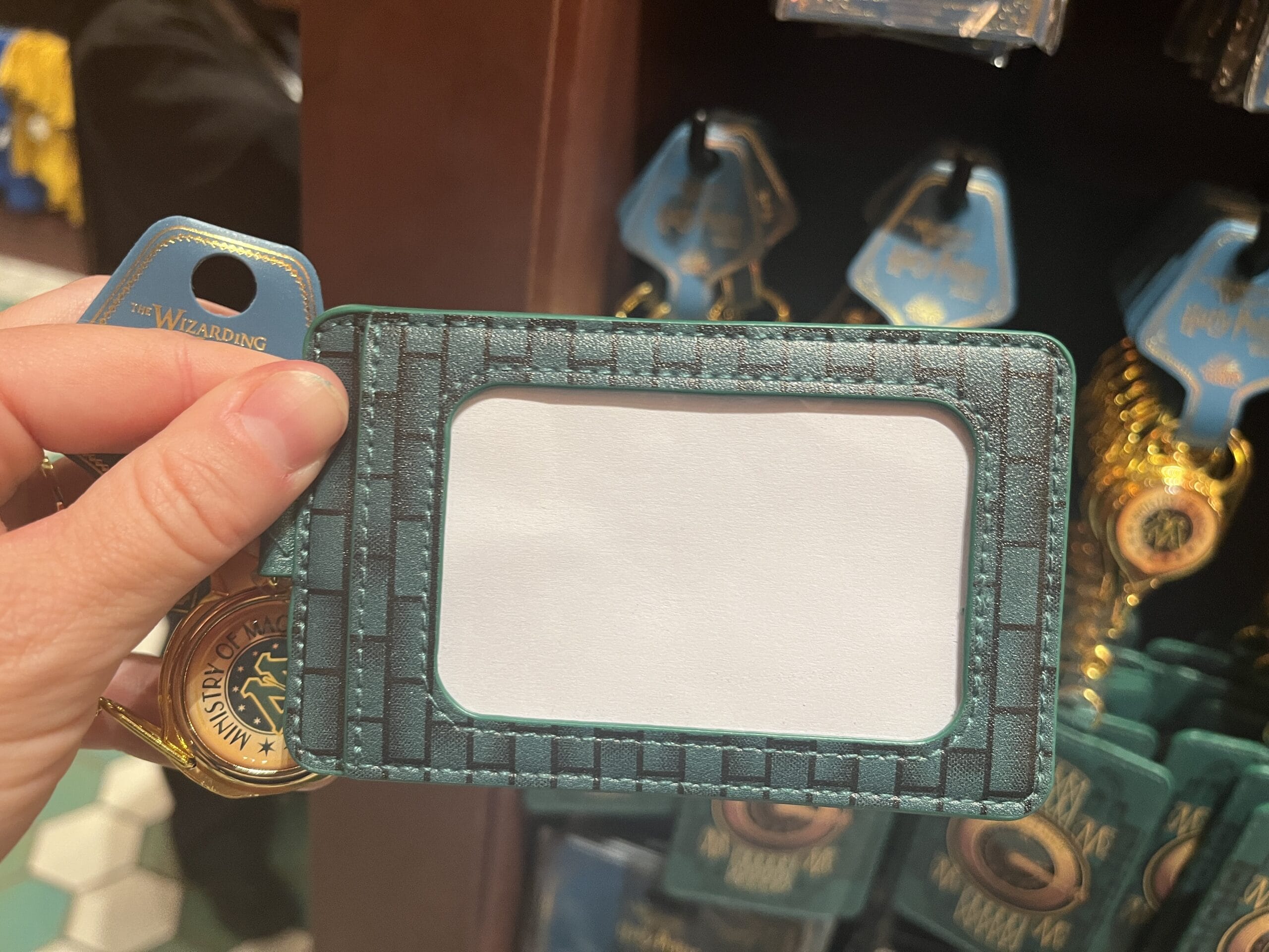 A hand holds a blank ID card holder in a store, with Wizarding World of Harry Potter merchandise in the background.