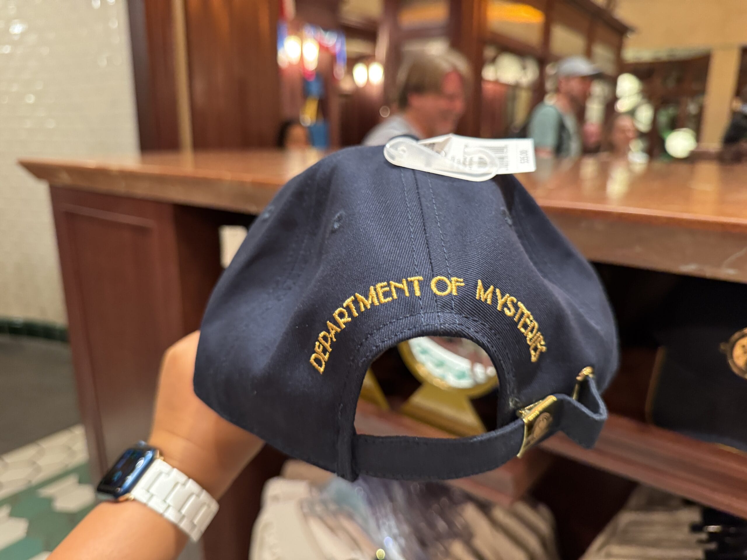 A hand holds a navy cap with “Department of Mysteries” in gold, exclusive Wizarding World of Harry Potter merchandise.