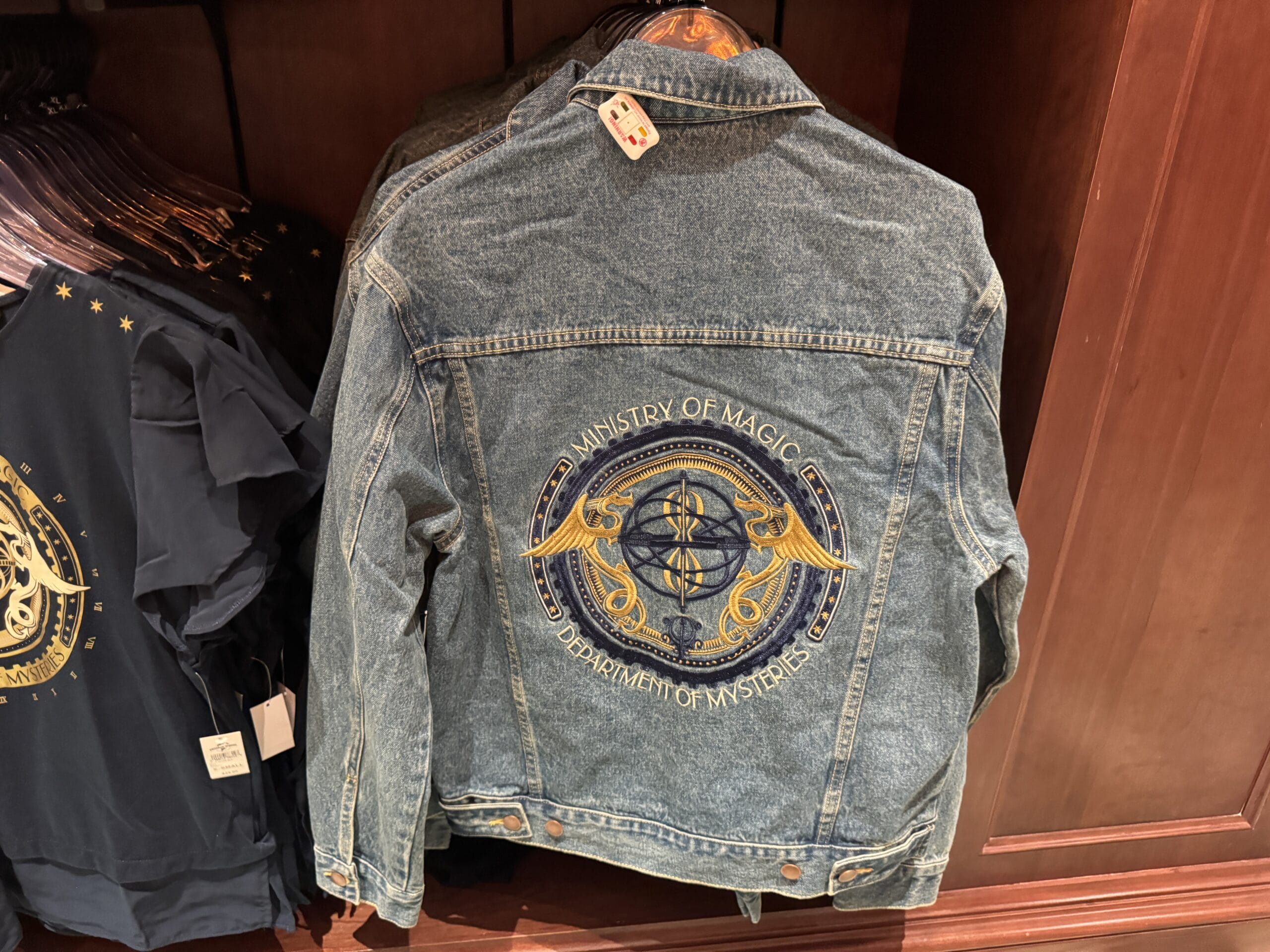 Blue denim jacket with a "Ministry of Magic Department of Mysteries" emblem—Epic Universe Wizarding World Harry Potter merchandise.