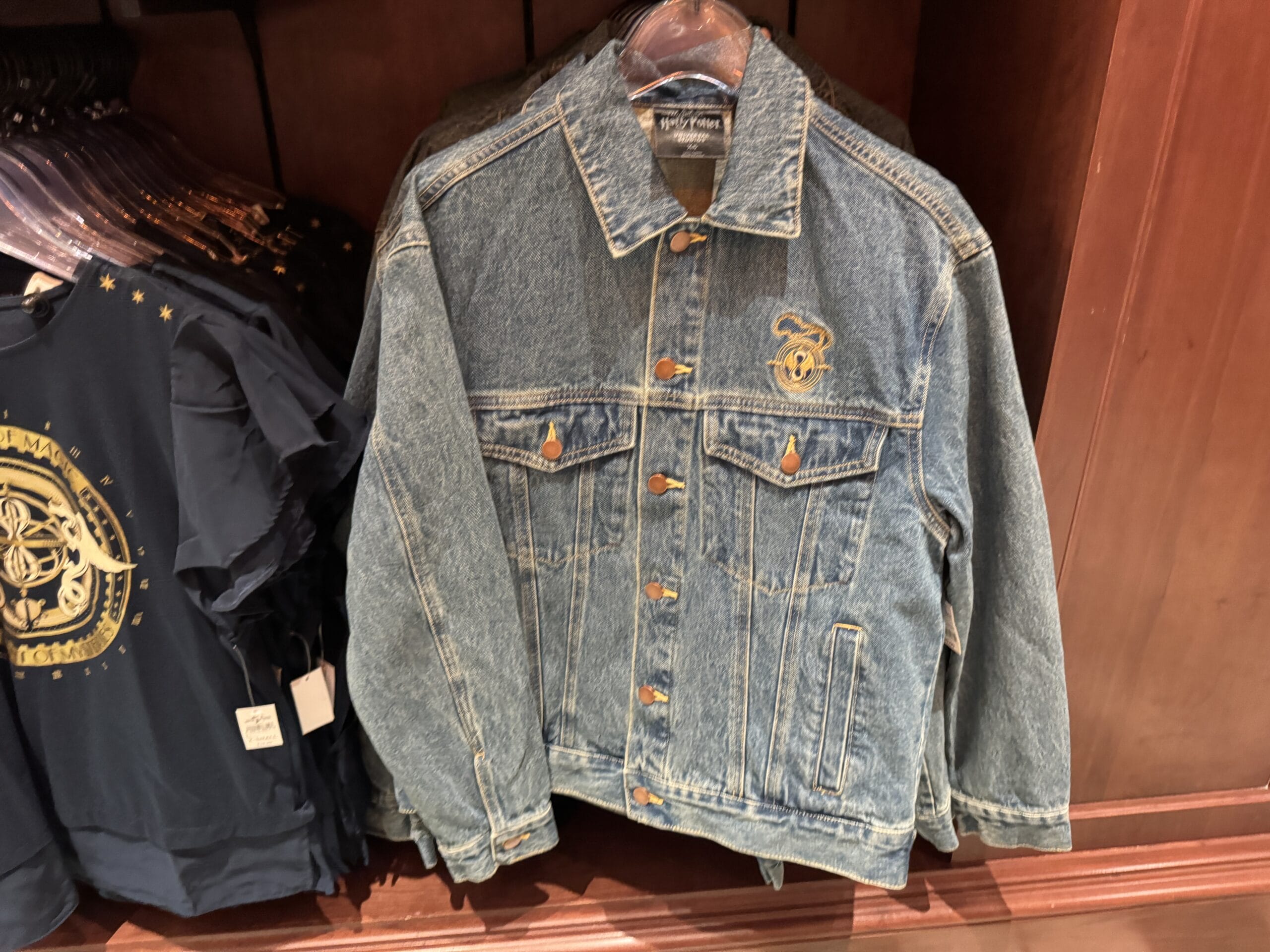 Blue denim jacket with gold patch, hanging beside navy graphic tees from the Wizarding World Harry Potter merchandise.