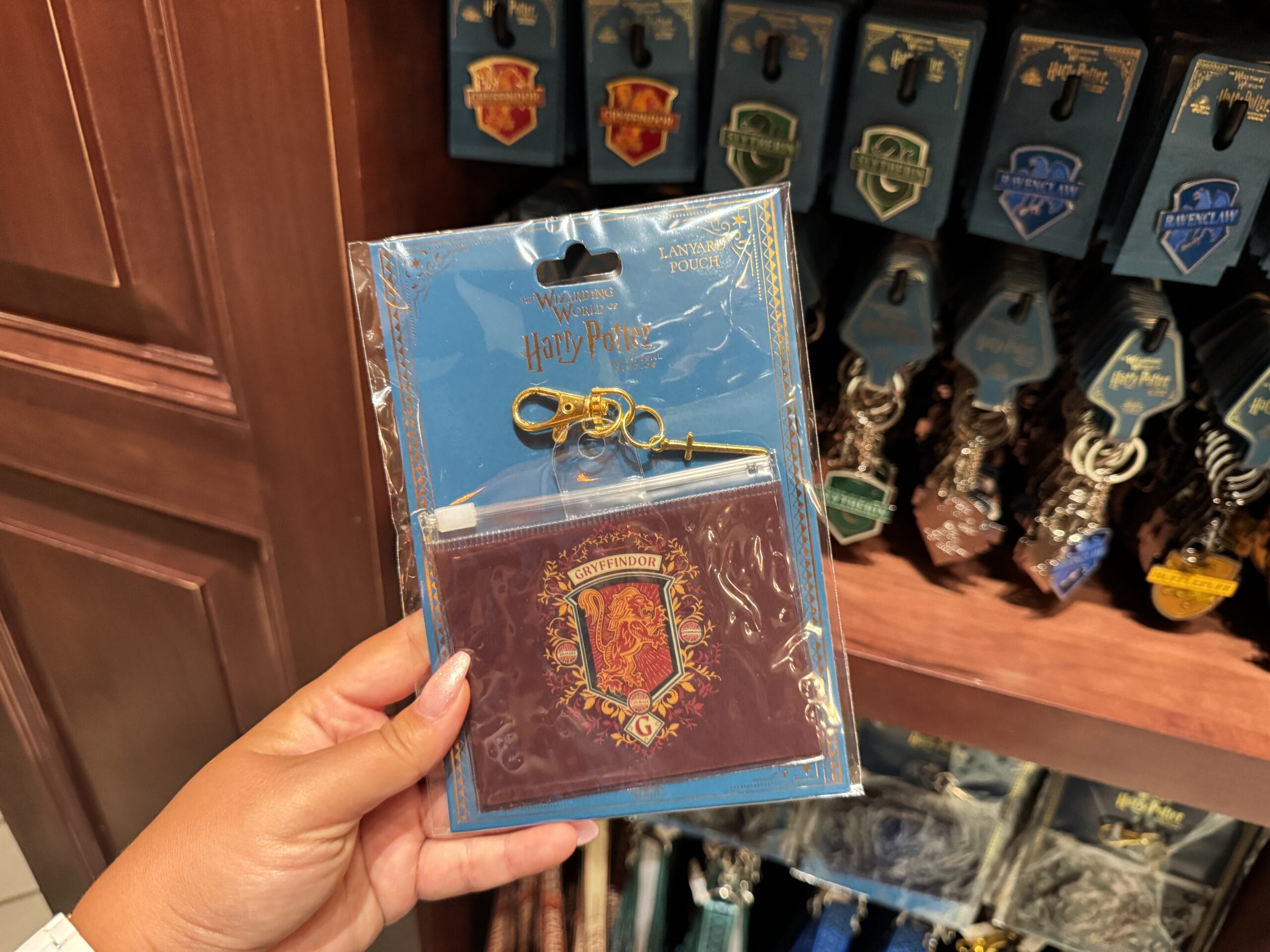 A hand holds a Gryffindor cardholder keychain from the Epic Universe Harry Potter merchandise in a store.