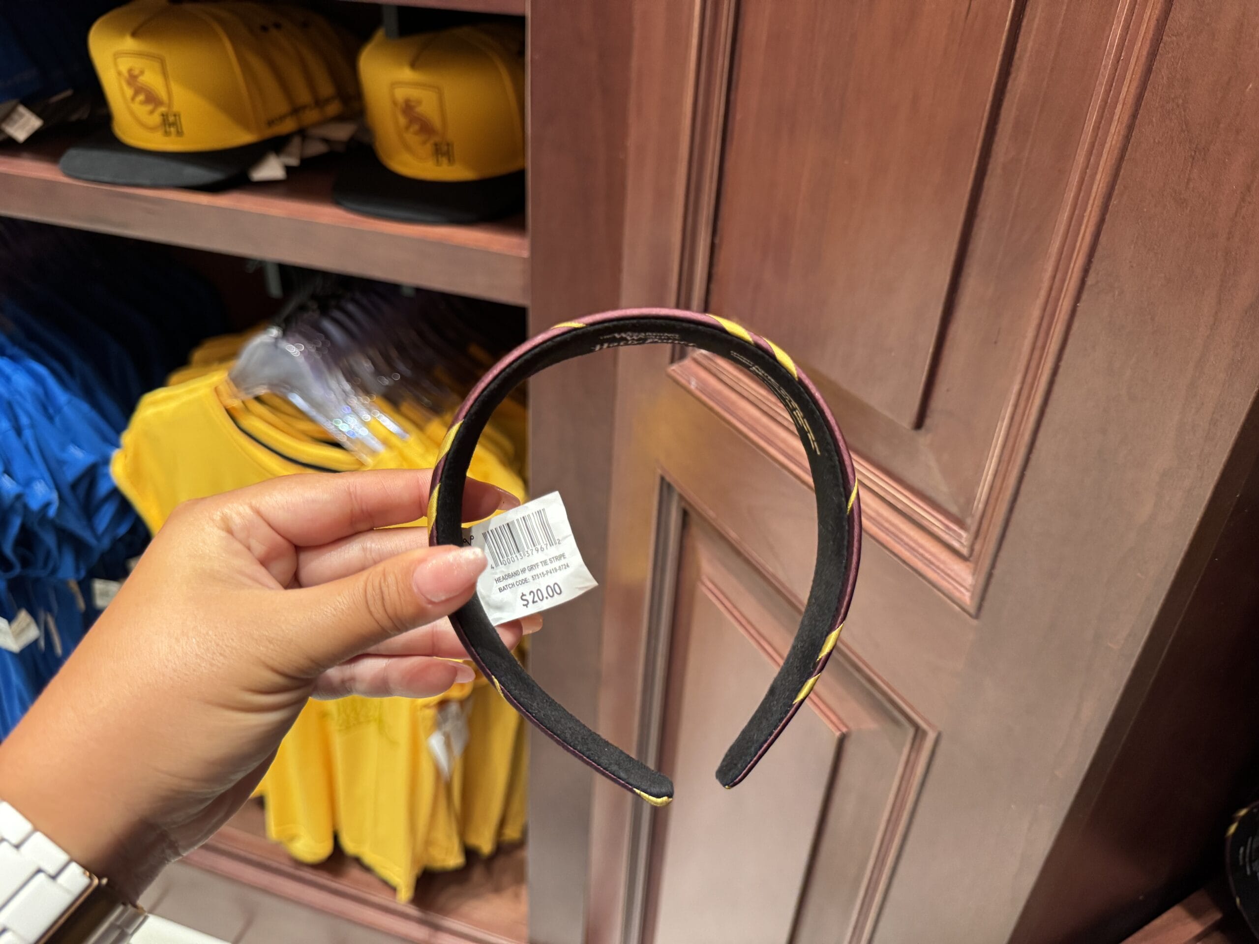 A hand holds Wizarding World of Harry Potter merchandise—a black and yellow headband with a $20 price tag in-store.