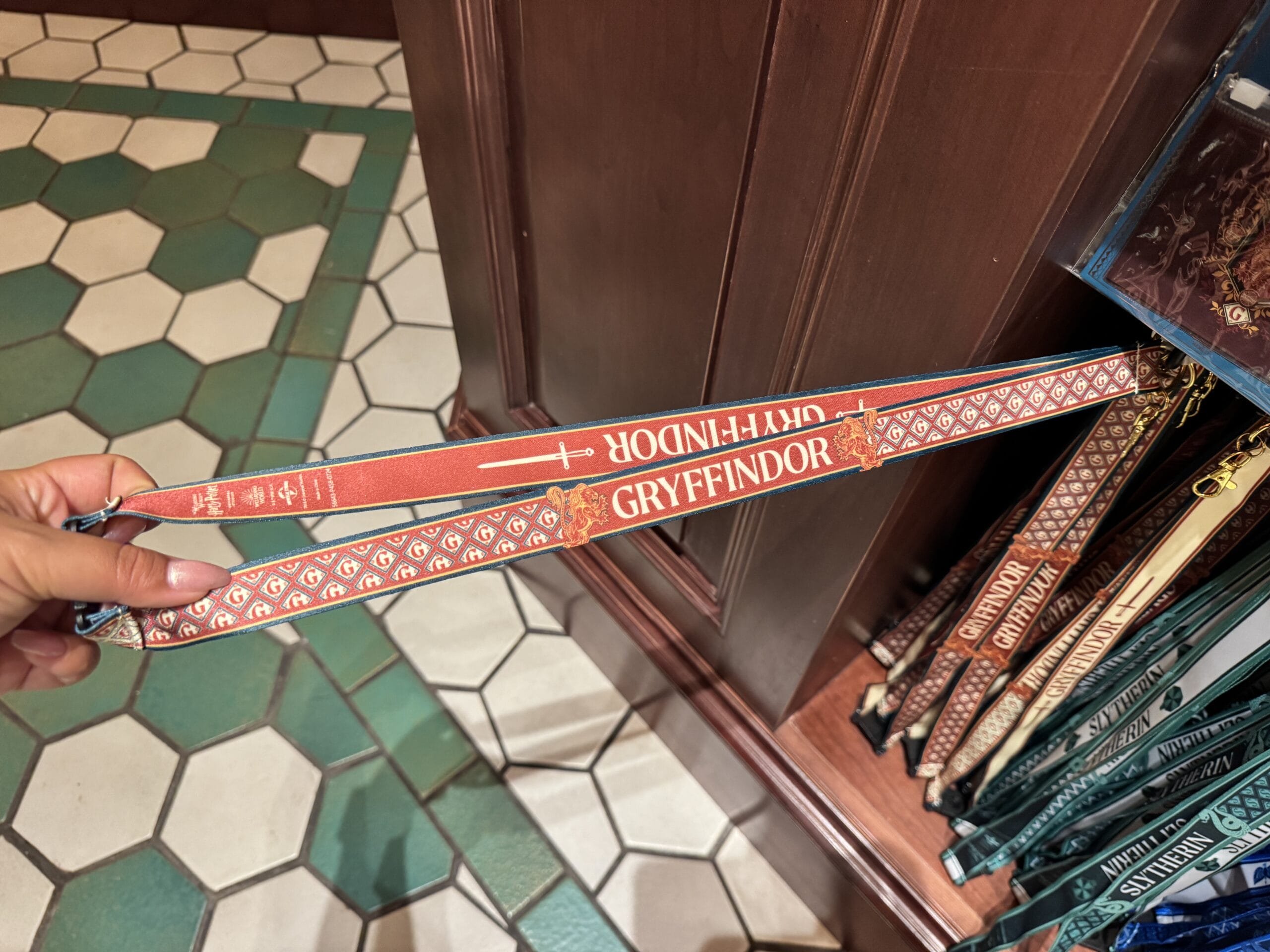 A hand holds a red Gryffindor lanyard, surrounded by Harry Potter merchandise in a store at Epic Universe.