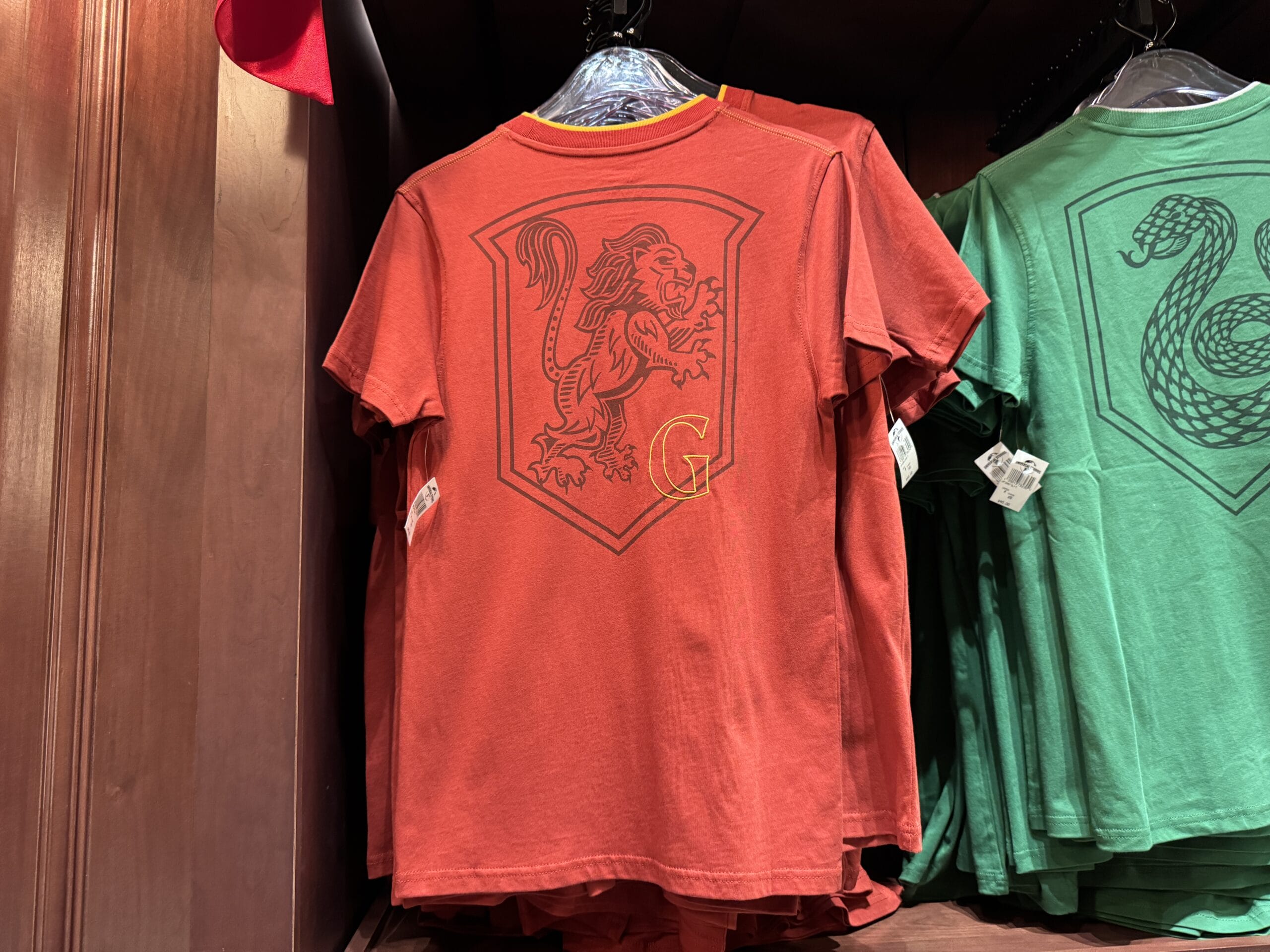 Red T-shirt with a lion crest and yellow "G"—Wizarding World of Harry Potter merchandise—next to a green serpent shirt.