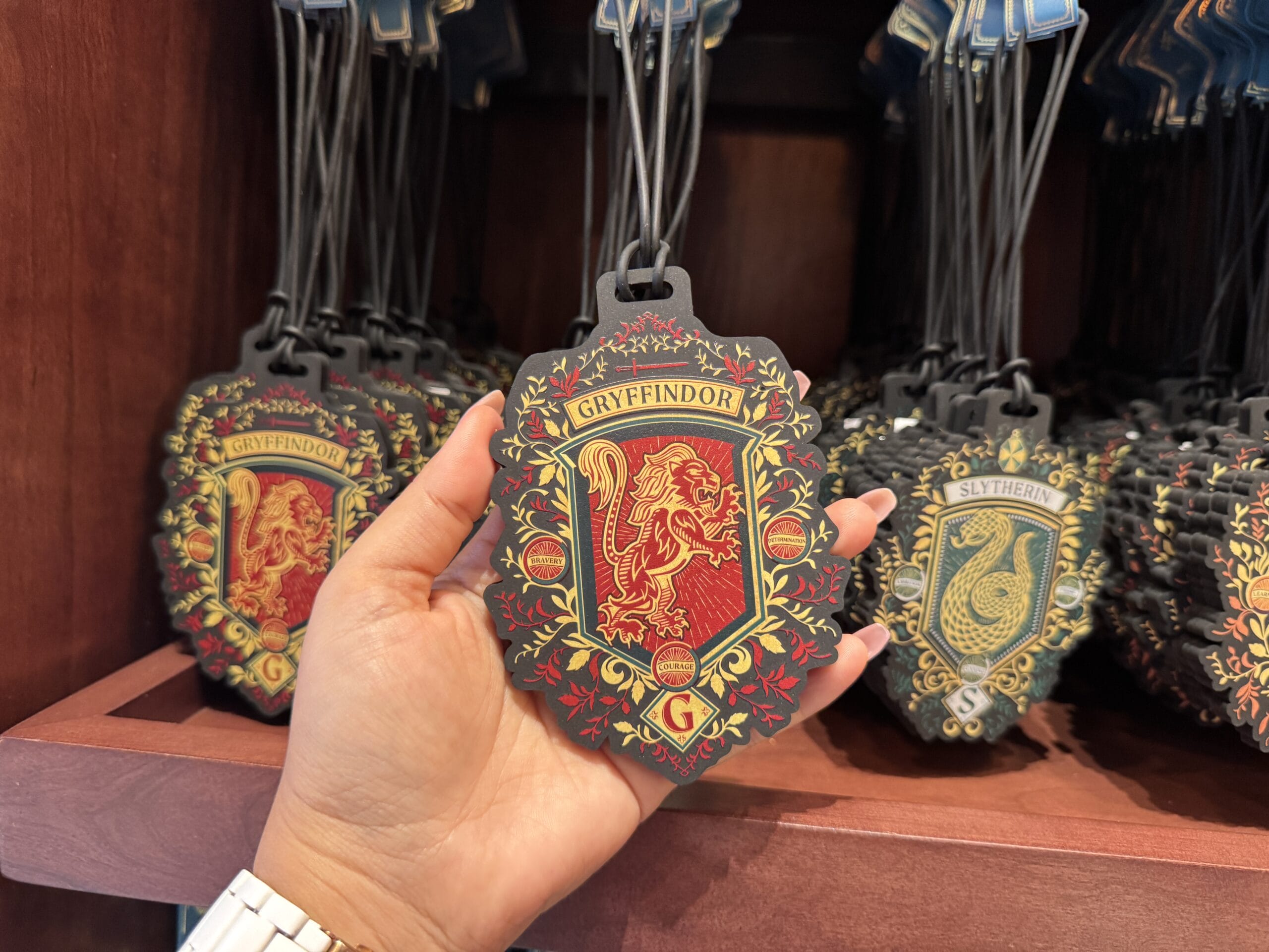A hand holds a Gryffindor crest keychain, part of Wizarding World of Harry Potter tour merchandise on display.