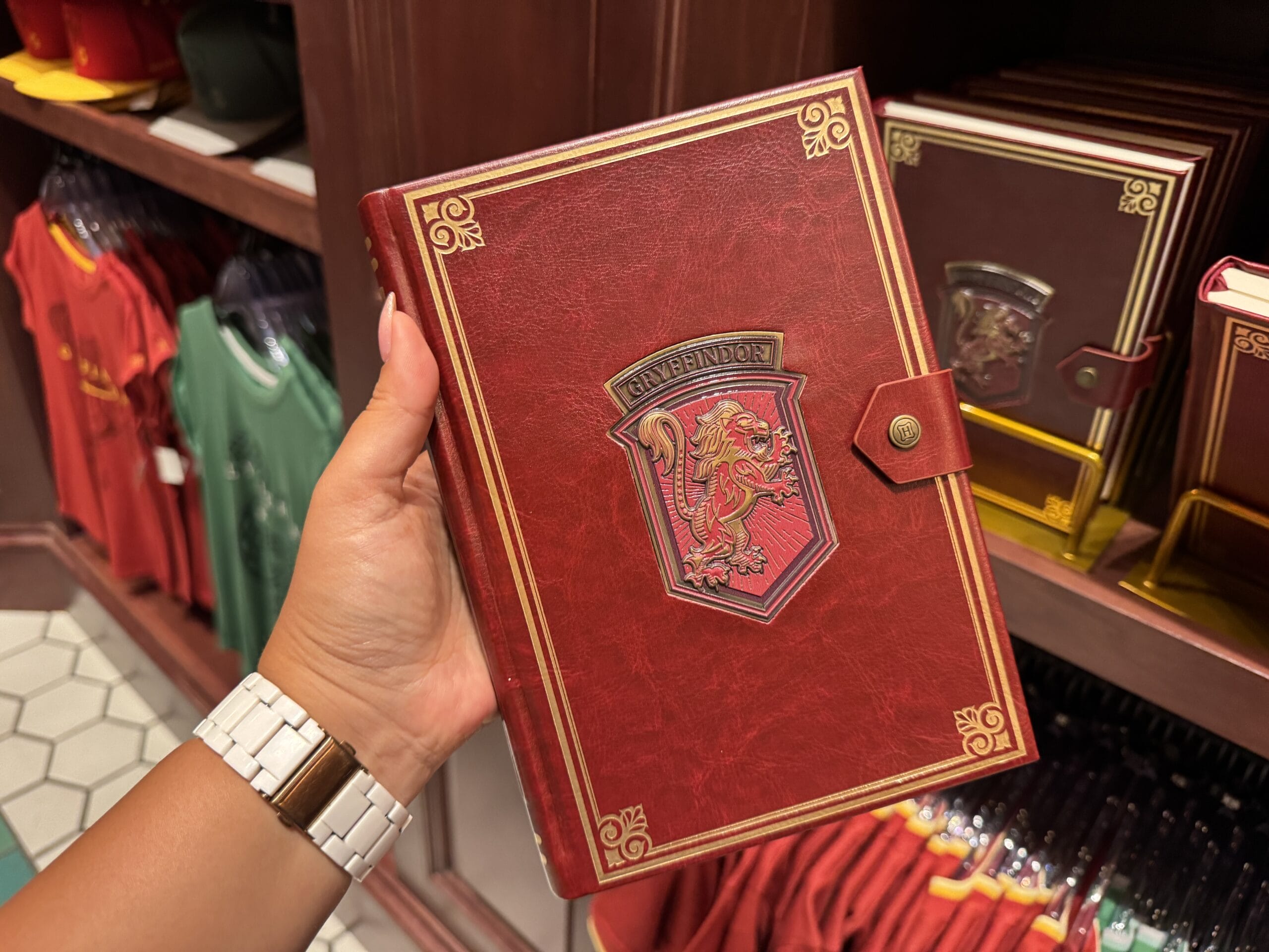 A hand holds a red Gryffindor notebook with gold details—magical Wizarding World merchandise found in a store.