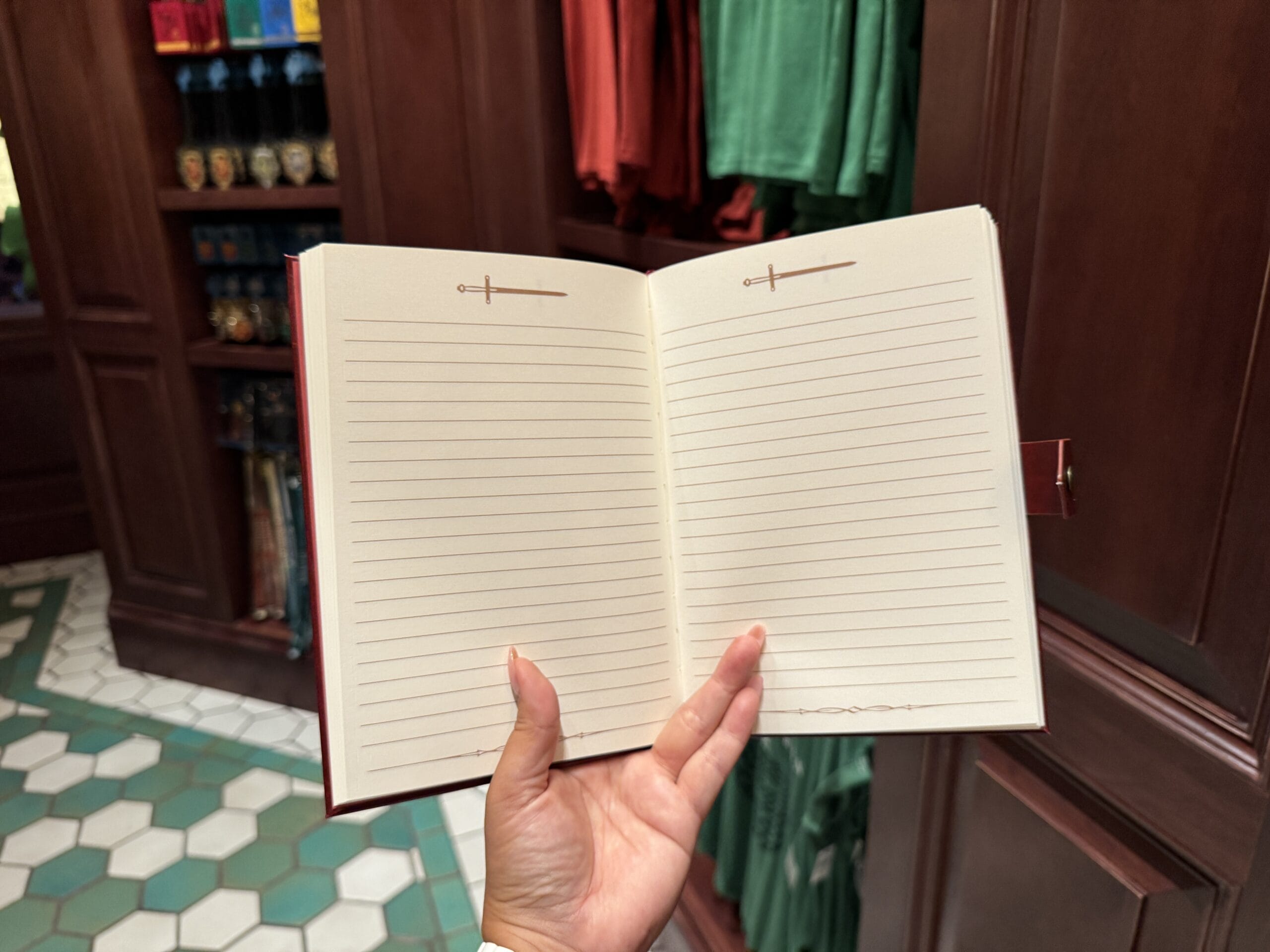 A hand holds a blank journal in a store with Tour En Floo merchandise and clothing on shelves in the background.