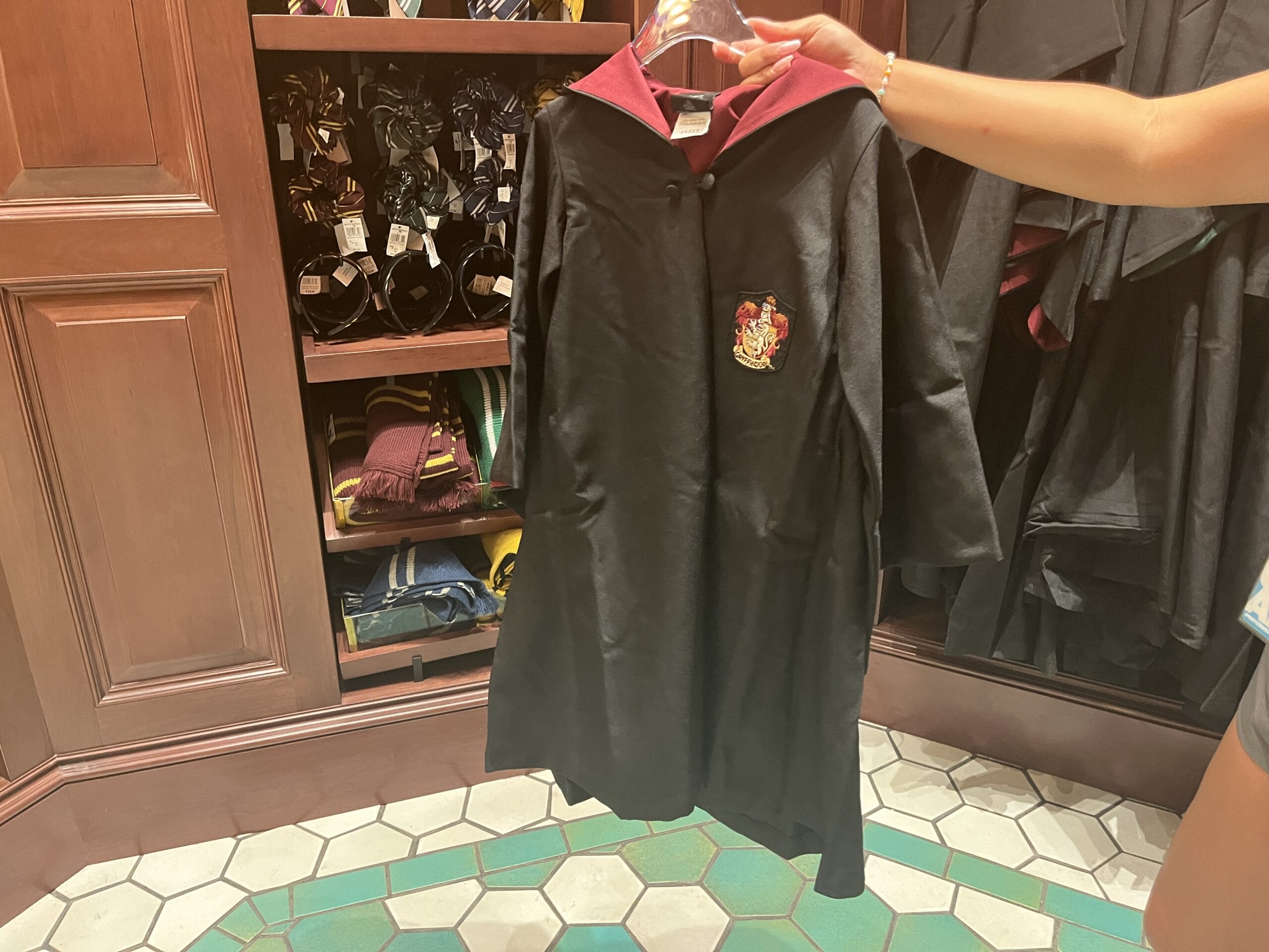 A person holds a black Gryffindor robe with a red hood in a store selling Epic Universe Harry Potter merchandise.