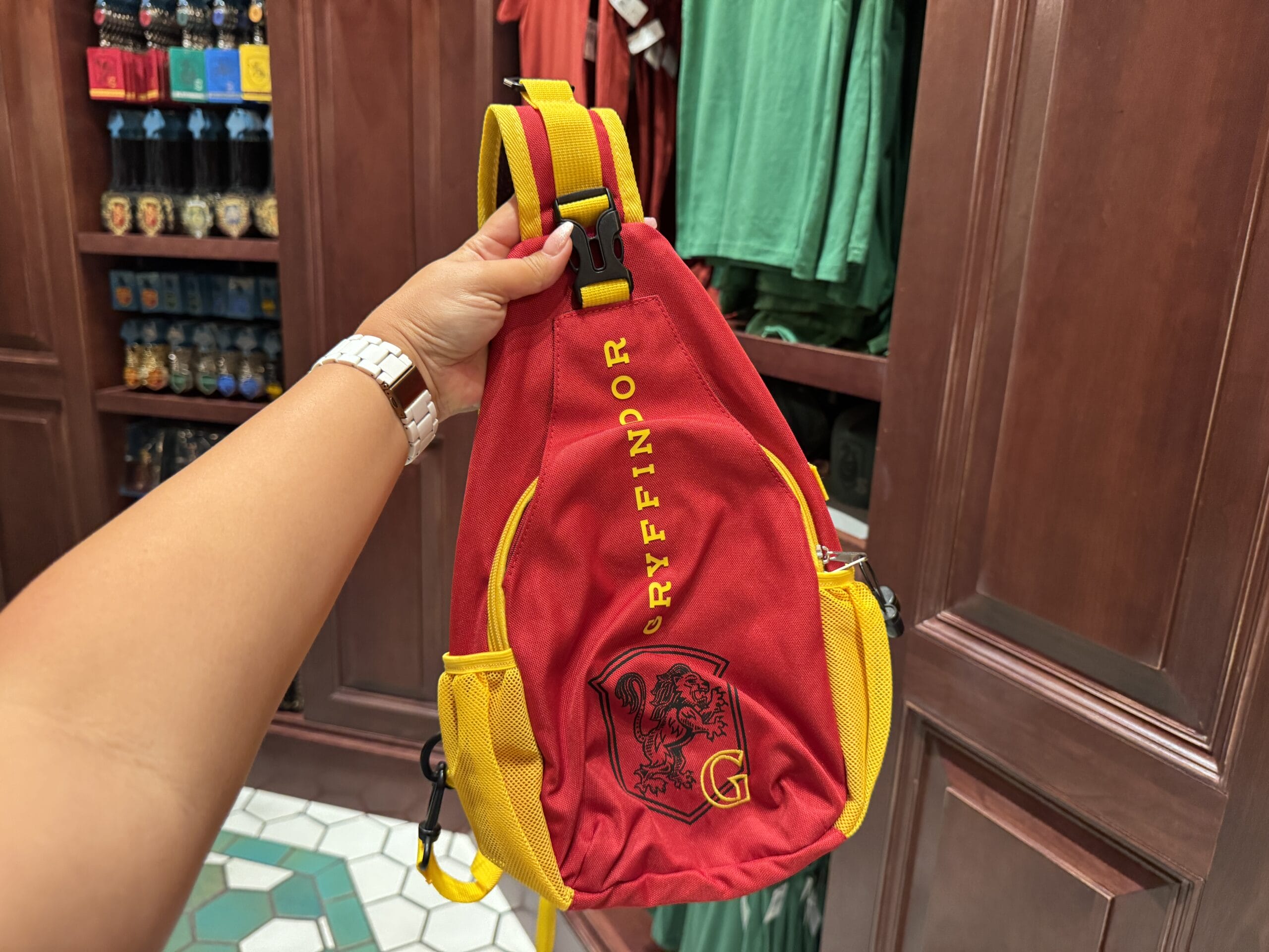 A person holds a Gryffindor sling bag with lion emblem from the Wizarding World of Harry Potter merch in a store.