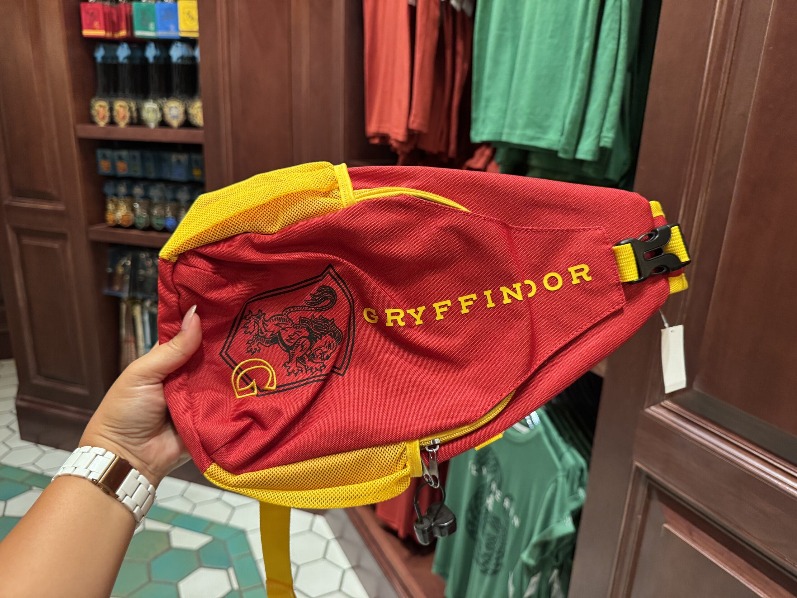 A hand holds a red and yellow Gryffindor fanny pack—Wizarding World of Harry Potter merchandise—in a store.