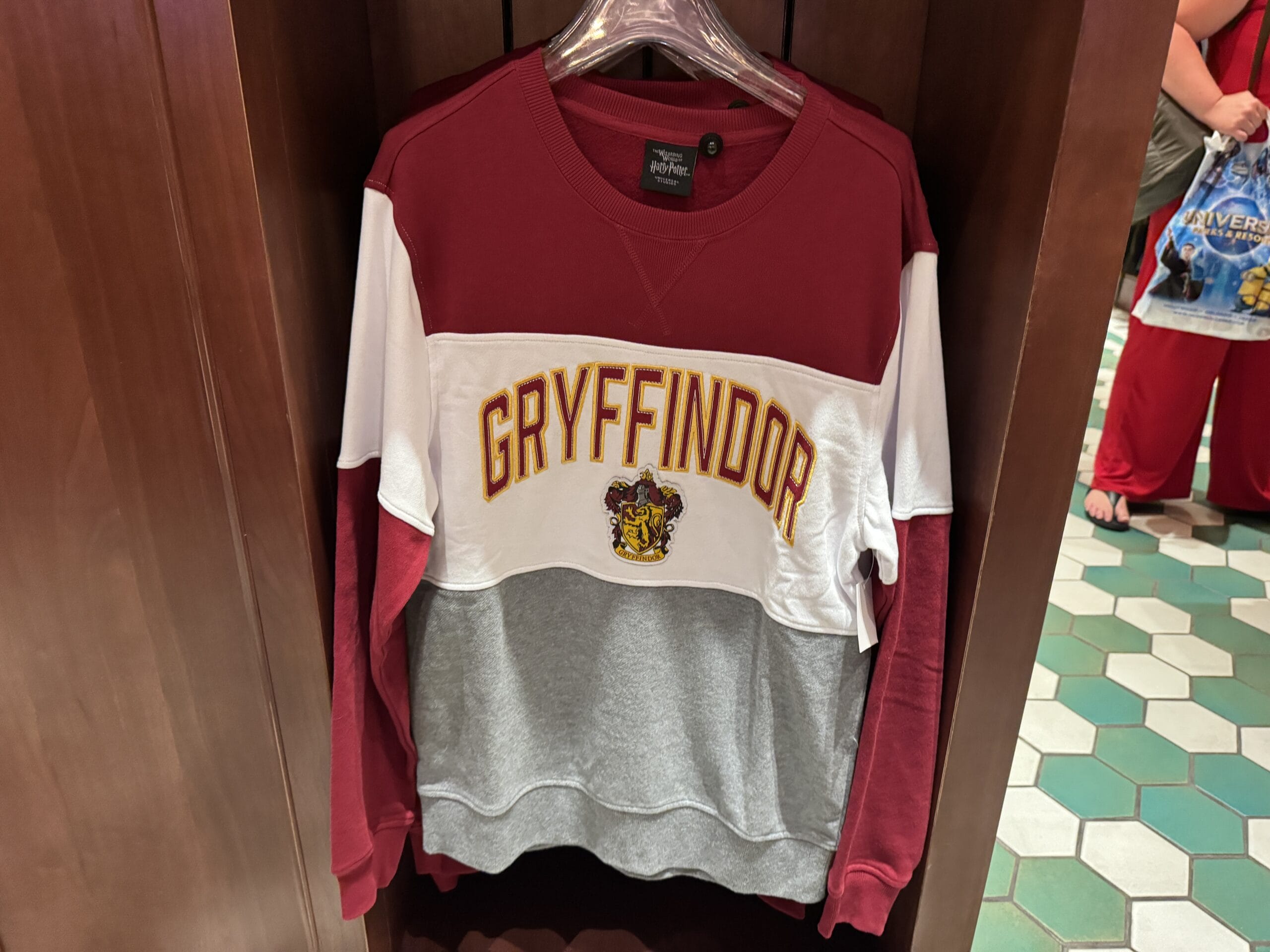 A Gryffindor sweatshirt from the Wizarding World of Harry Potter merchandise hangs on a clear hanger in a store display.