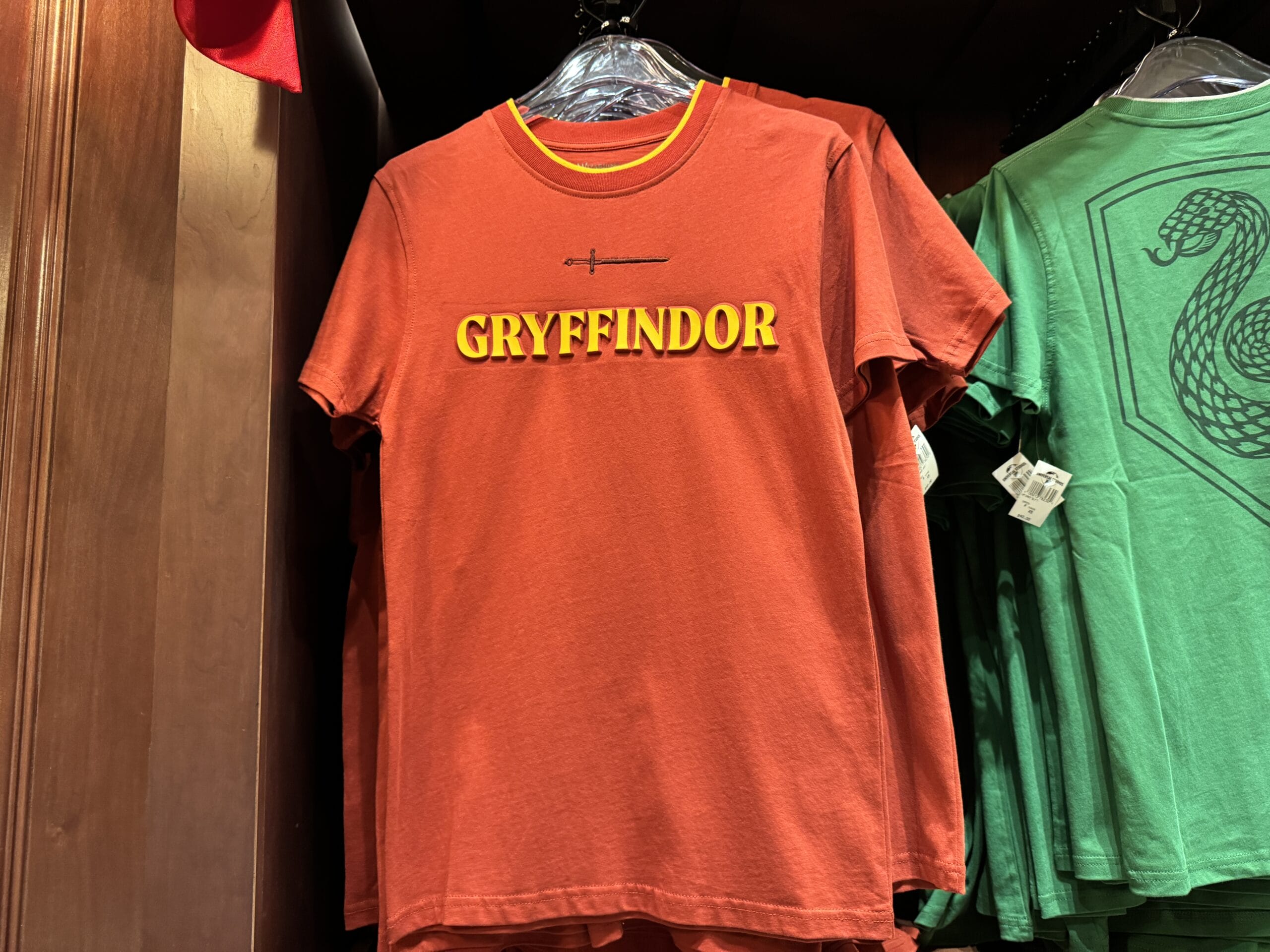 Red t-shirt with "Gryffindor" and a sword—official Wizarding World of Harry Potter merchandise, on a clothing rack.