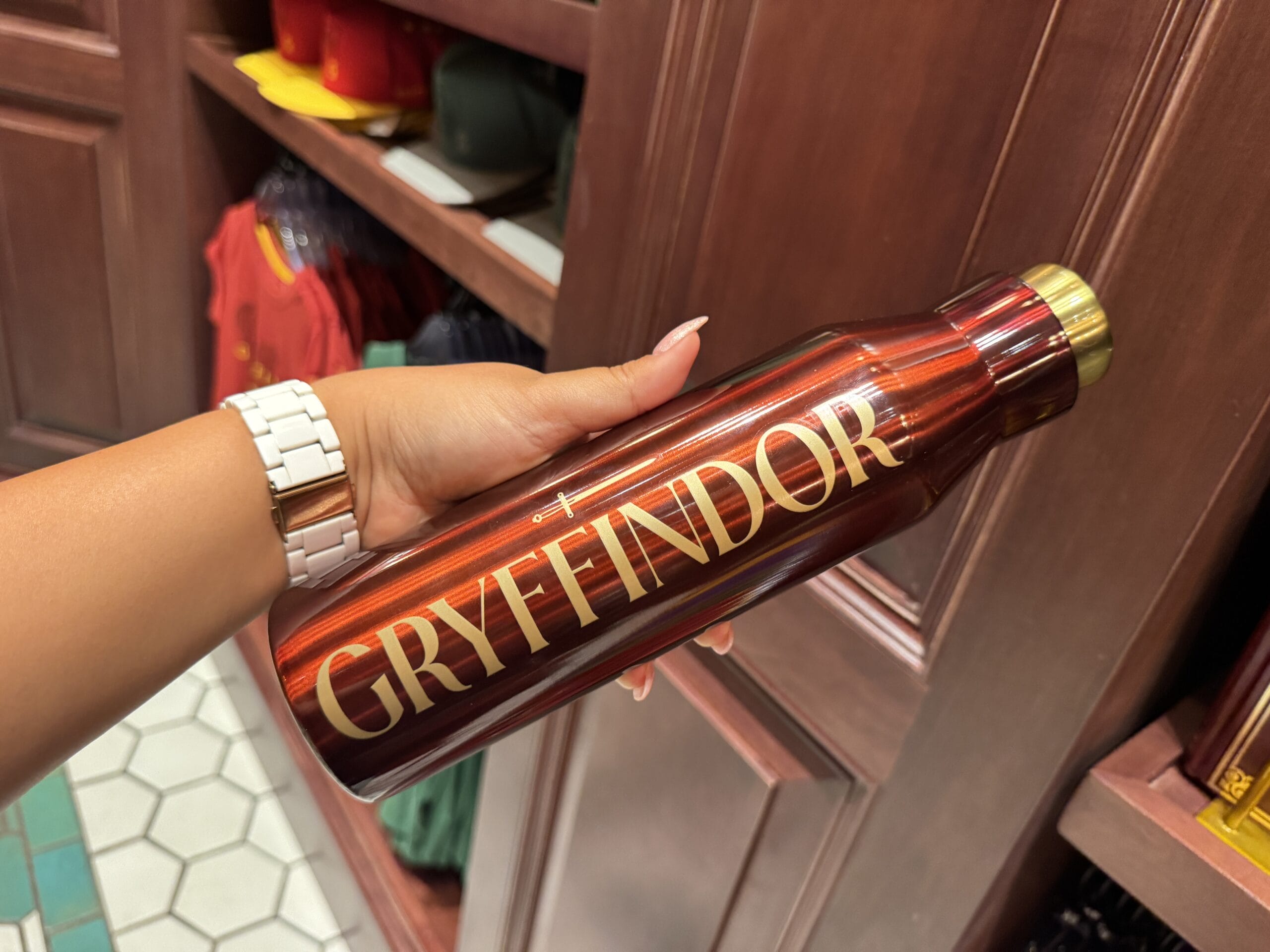 A hand holds a metallic red water bottle with "GRYFFINDOR" in gold—perfect Harry Potter merchandise for Wizarding World fans.