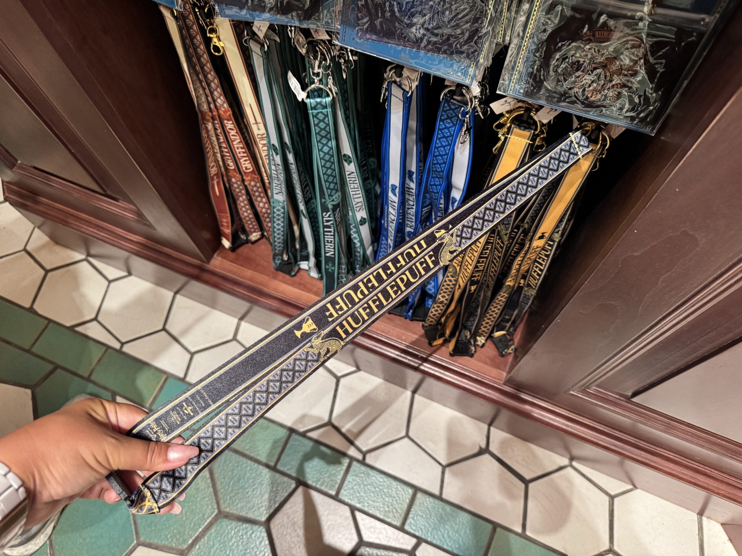 A hand holds a "Hufflepuff" lanyard amid Wizarding World of Harry Potter merchandise displays.
