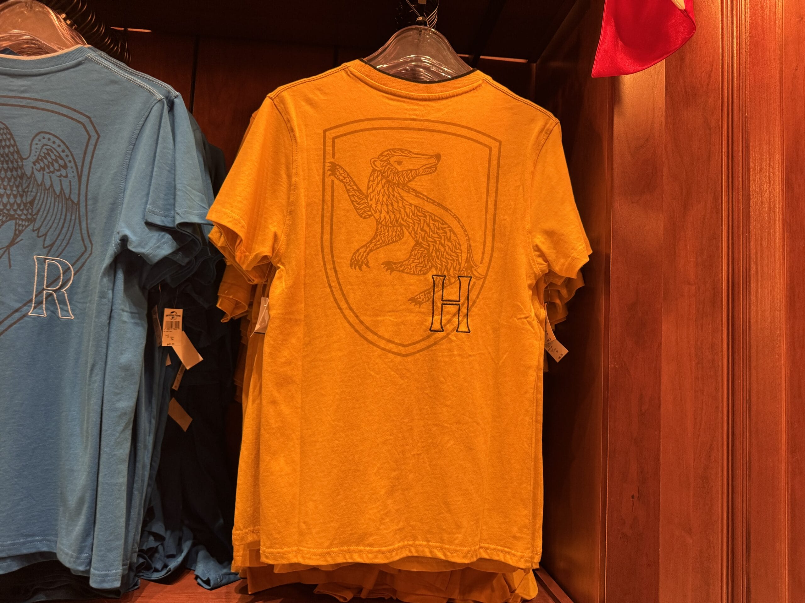 A yellow t-shirt with a badger emblem and "H" on the back, perfect for Harry Potter merchandise collectors.