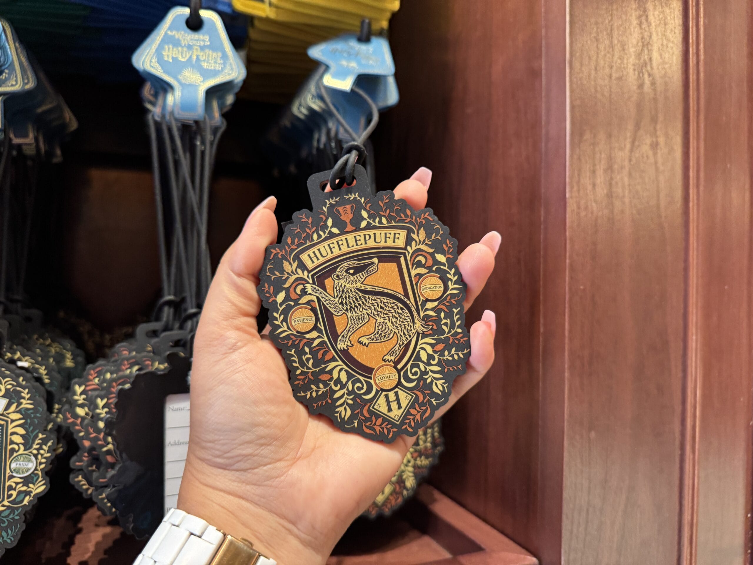 A hand holds a decorative Hufflepuff crest ornament at the Wizarding World of Harry Potter merchandise display.